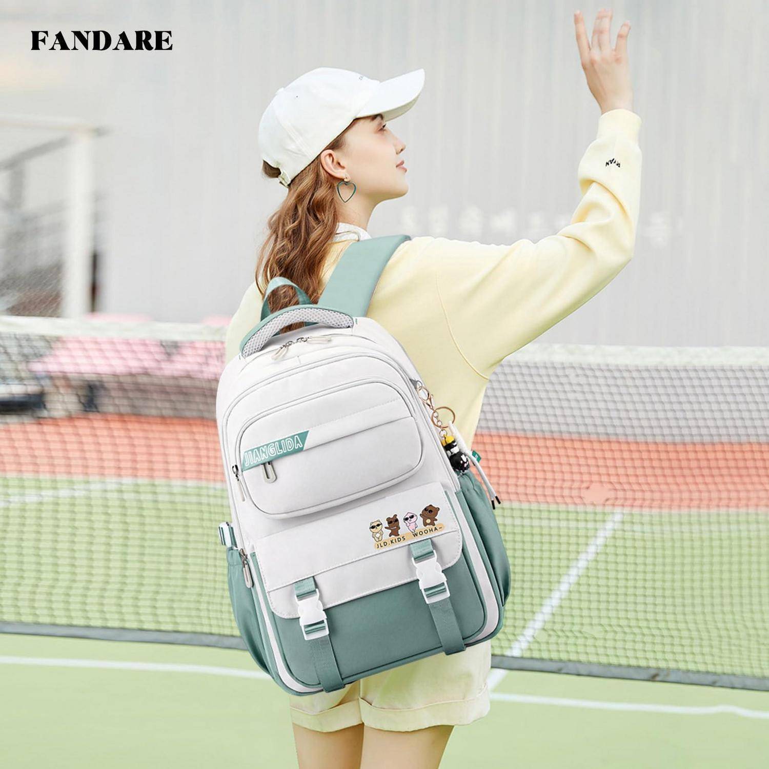 Junge Frau mit weißer Mütze und Pastelloutfit zeigt einen weiß-mintfarbenen Rucksack auf einem Tennisplatz.