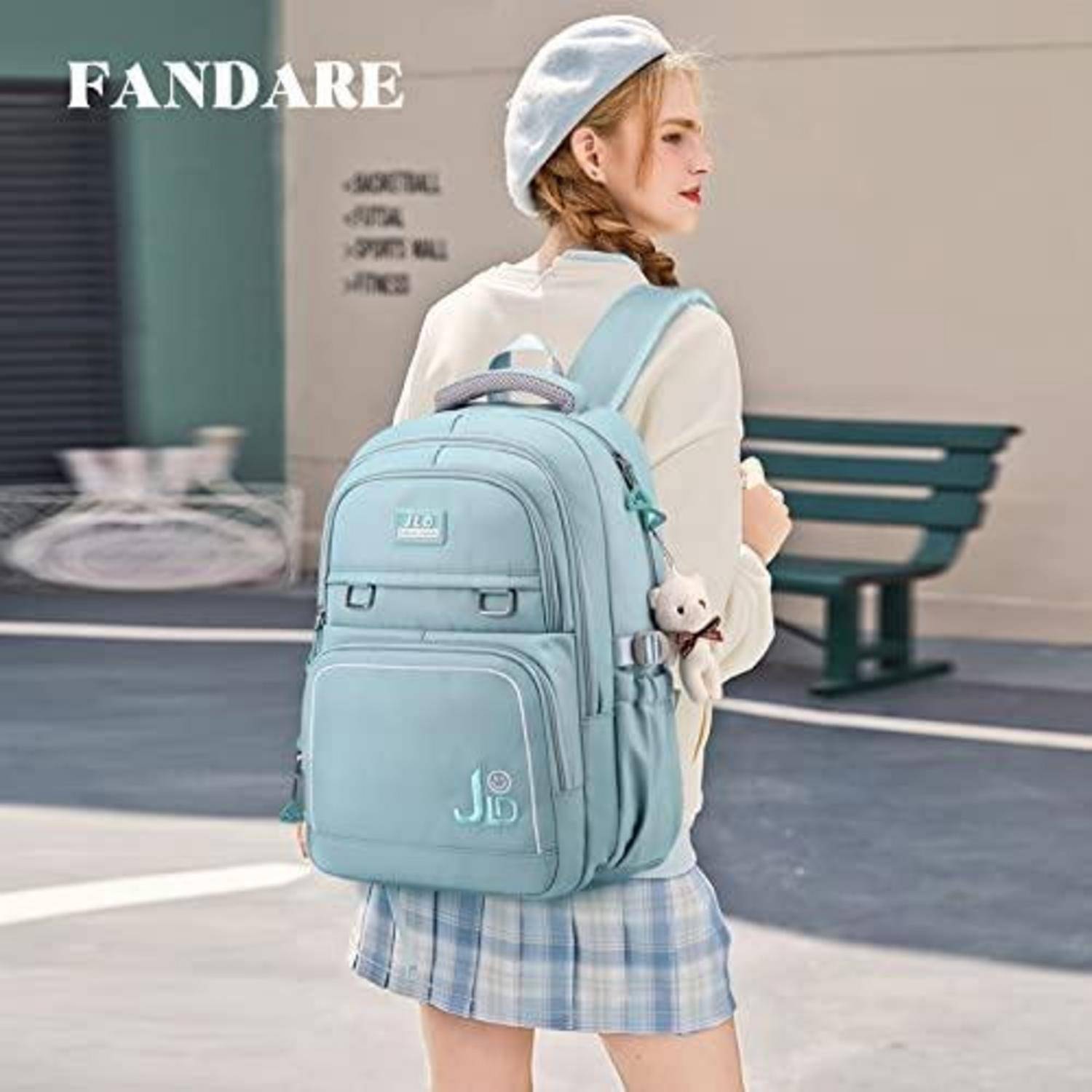 Mädchen, das einen hellblauen Rucksack mit Teddybär-Anhänger trägt, in Profilansicht im Freien in der Nähe einer Bank; FANDARE-Logo oben links.