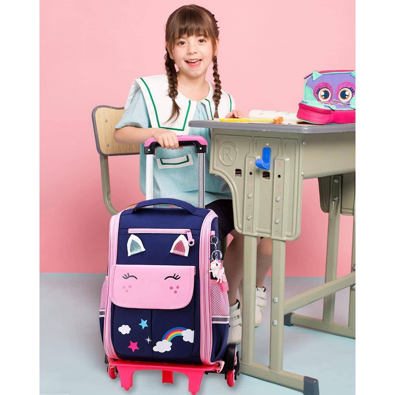 Junge Schülerin sitzt an einem Schreibtisch mit einem großen rosa-dunkelblauem Rucksack auf Rollen davor, vor einem rosa Studiohintergrund.