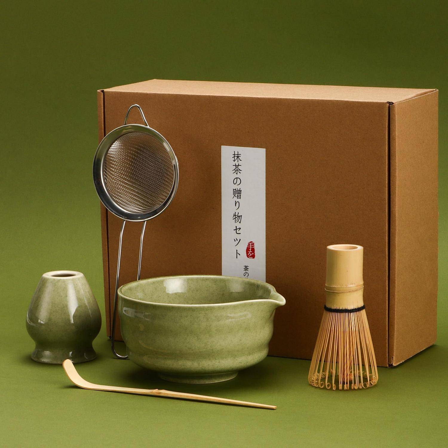 Matcha-Tee-Set mit Schale, Besen, Sieb, Löffel und Kanne vor einer beschrifteten Kartonbox.