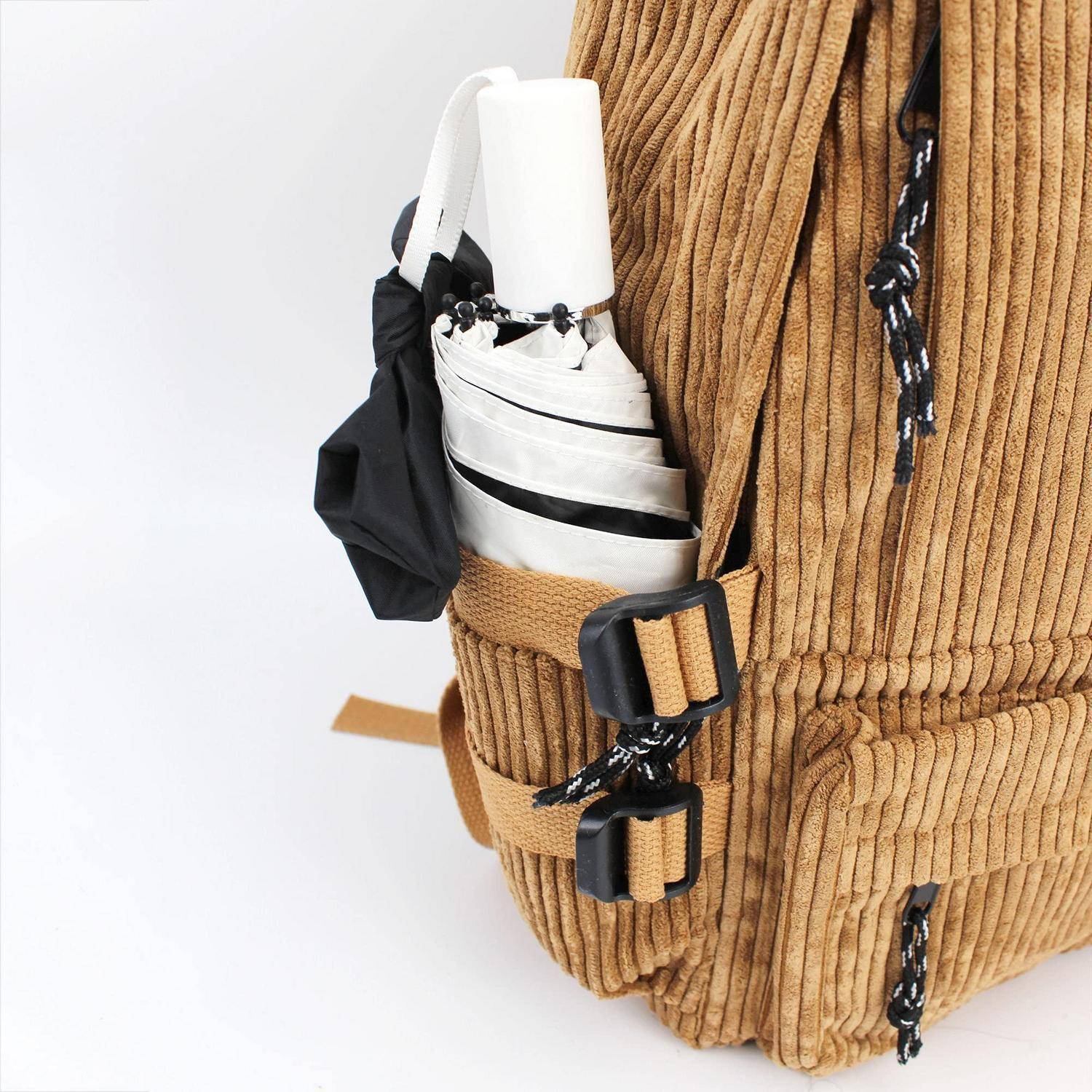 Nahaufnahme einer beigefarbenen Kord-Rucksack-Seitentasche, in der ein gefalteter weißer Regenschirm mit schwarzen Akzenten und Schnallen aufbewahrt wird.