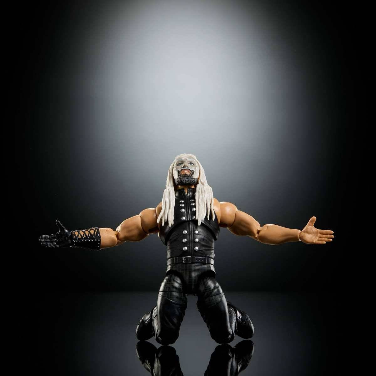 Actionfigur eines knienden Ringers mit langem weißem Haar und ausgestreckten Armen vor dunklem Studiohintergrund.