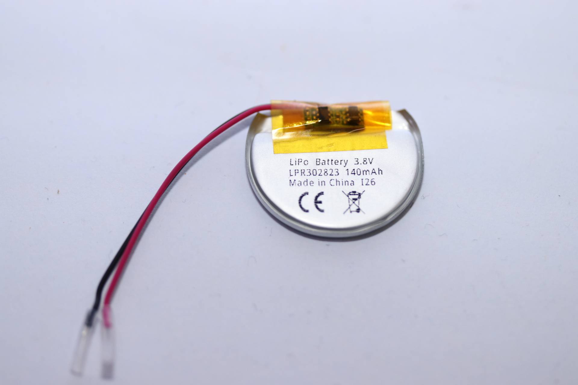Kleine runde 3,8V LiPo-Batterie mit roten und schwarzen Drähten und einem gelb geklebten Stecker auf einfachem Hintergrund.