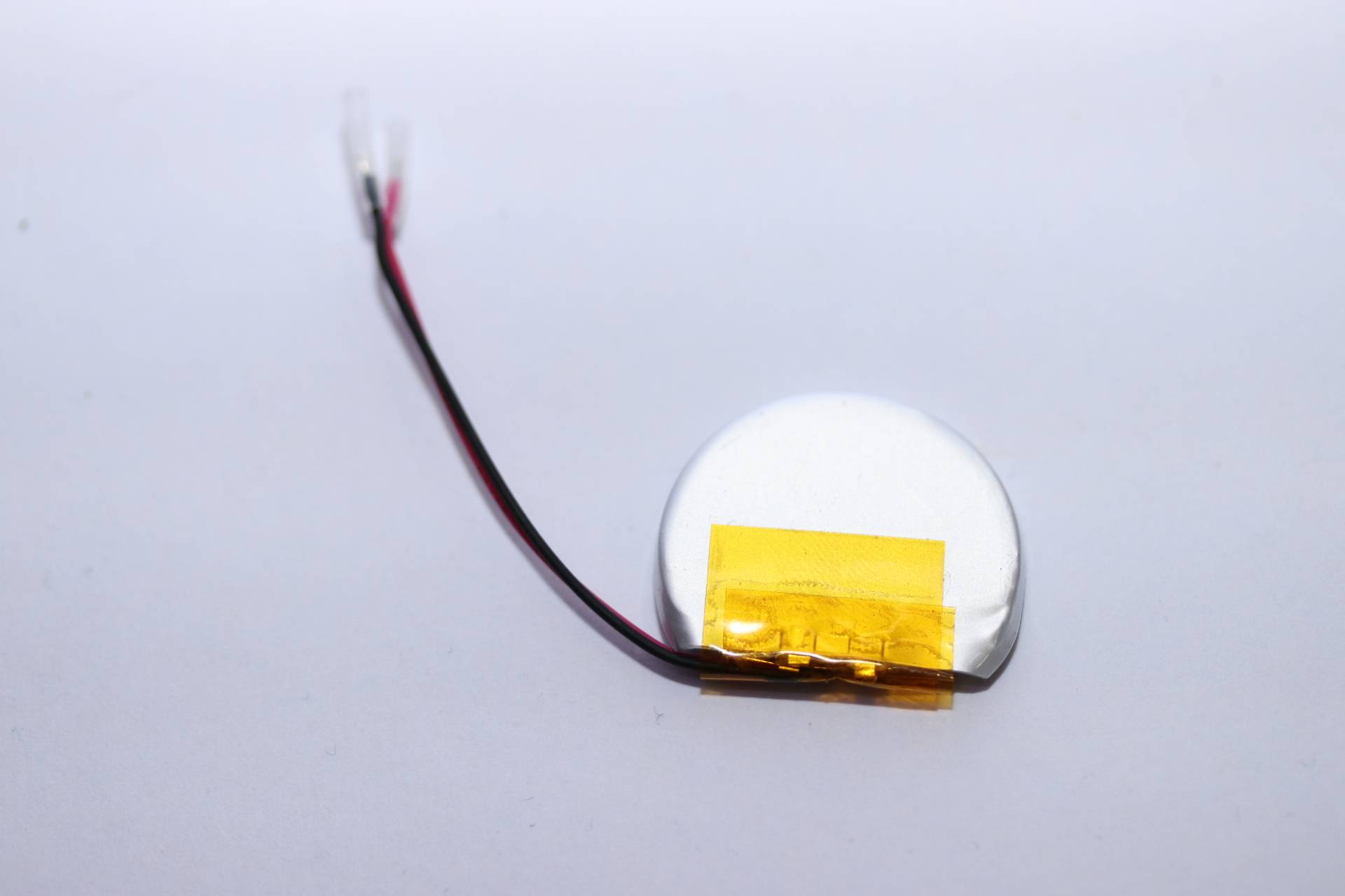 Kleine runde Knopfzellenbatterie mit roten und schwarzen Drähten auf hellem Hintergrund.