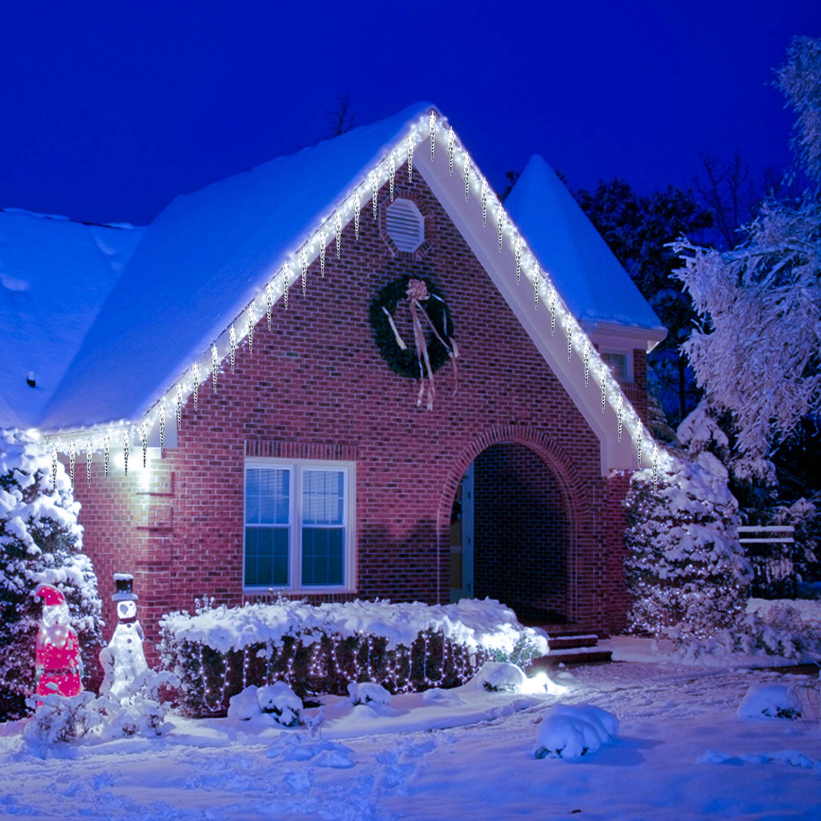 Schneebedecktes Backsteinhaus in der Nacht, dekoriert mit weißen Weihnachtslichtern, einem Kranz und beleuchteten Schneemännerfiguren im vorderen Garten.
