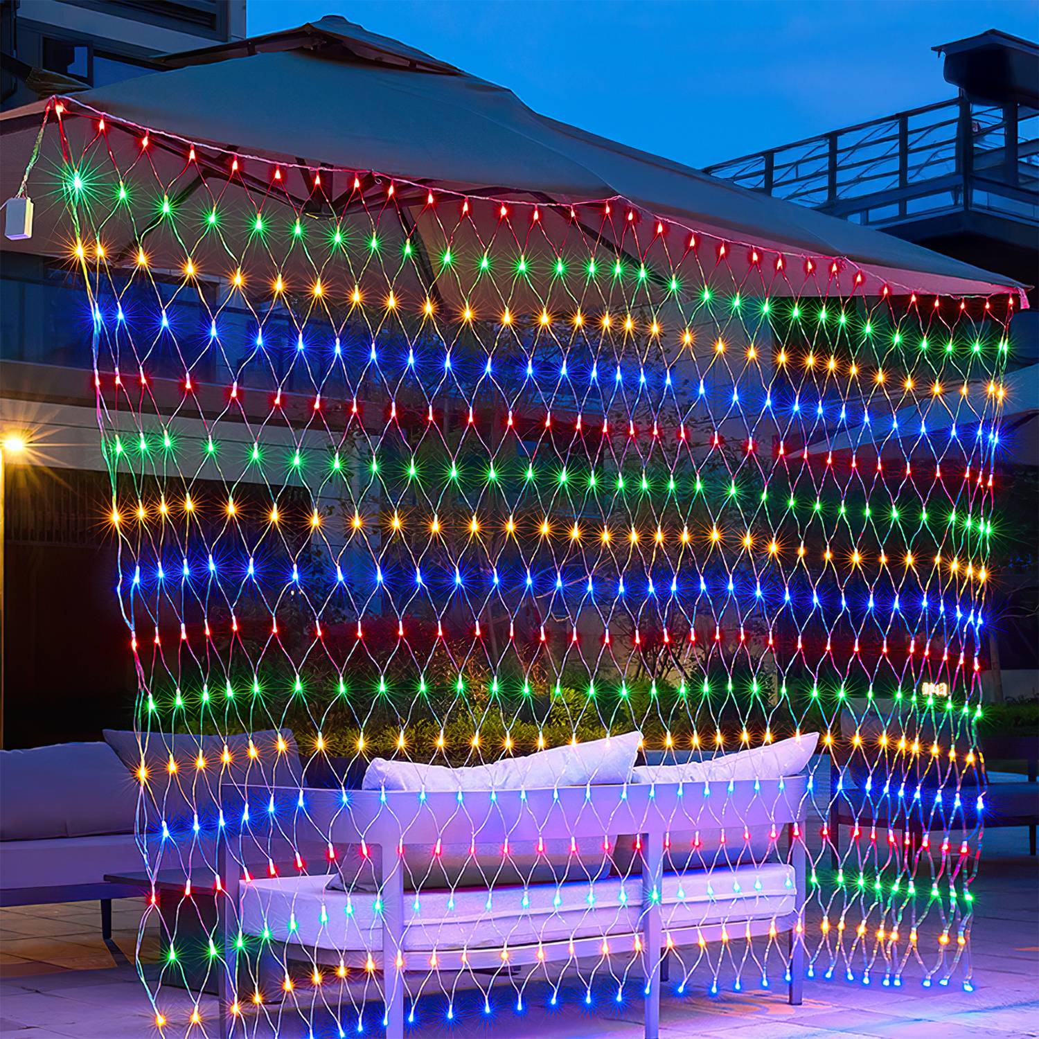 Bunte LED-Lichterkette als Vorhang, die über einem Außenpatio-Sofa in der Abenddämmerung hängt und einen dekorativen beleuchteten Hintergrund schafft.