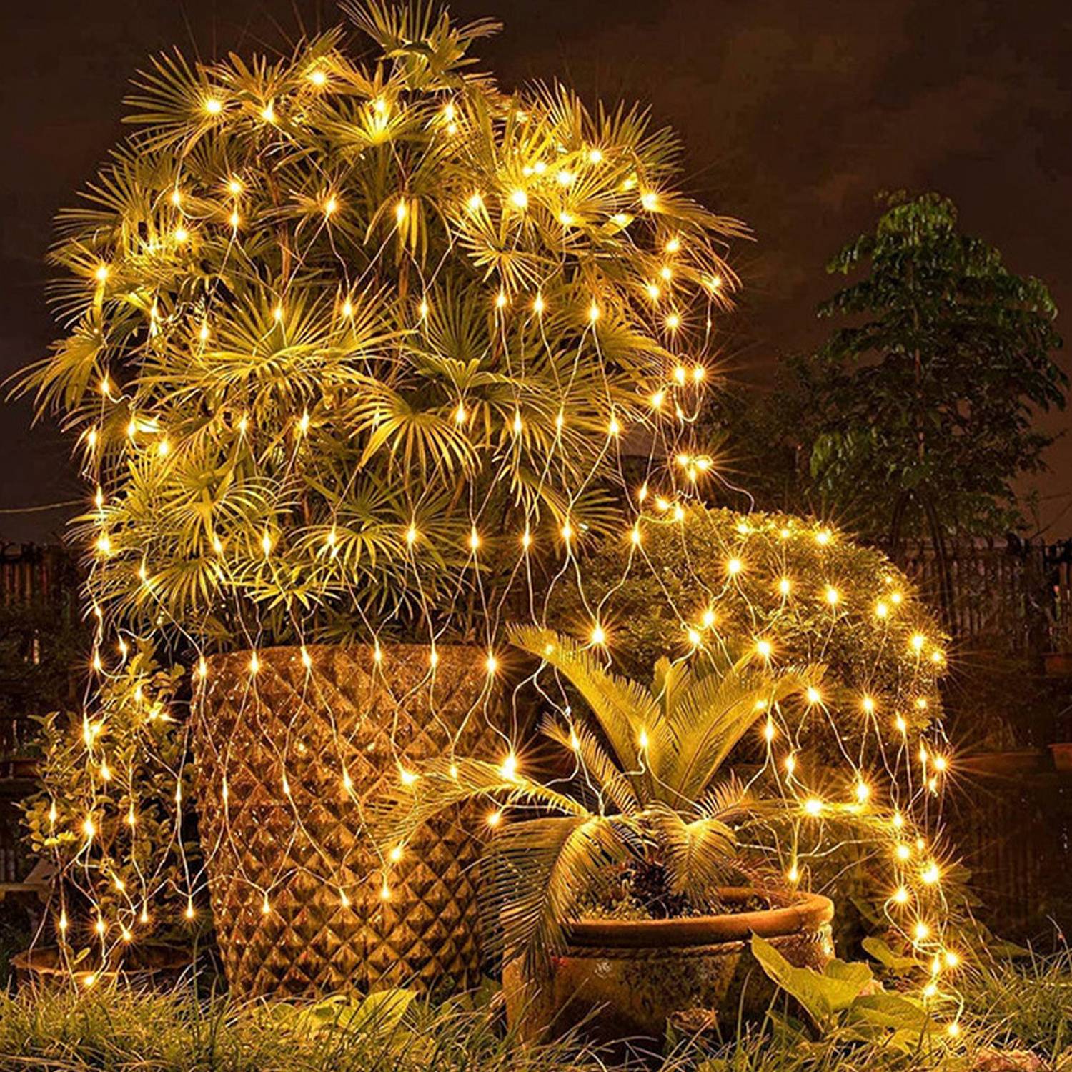 Goldene Feuerwerke platzen über einer Gartenausstellung in der Nacht auf und beleuchten Topfpflanzen und einen geflochtenen Blumenkasten.