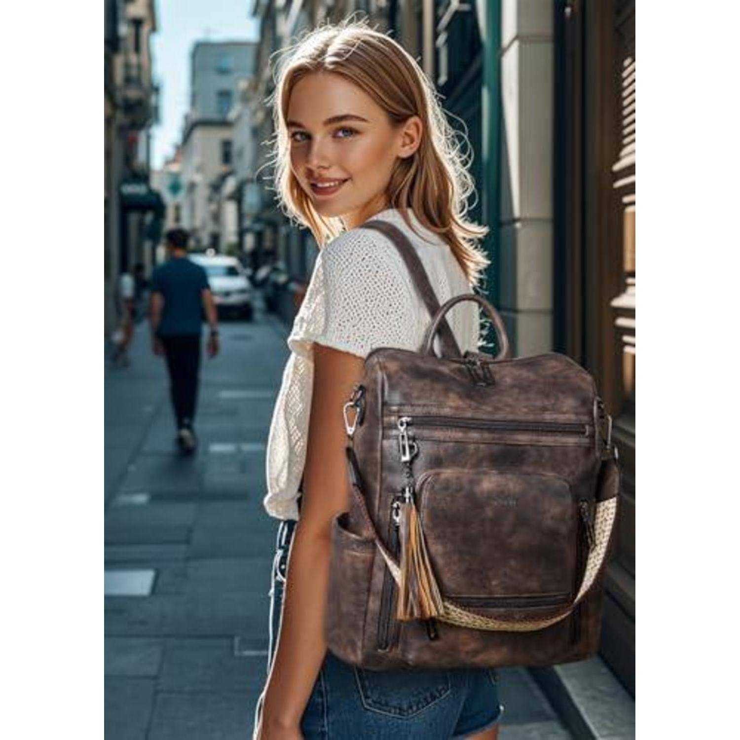 Junge Frau auf einer Stadtstraße, die über ihre Schulter zurückblickt, trägt ein weißes Oberteil und Jeans mit einem braunen Lederrucksack.