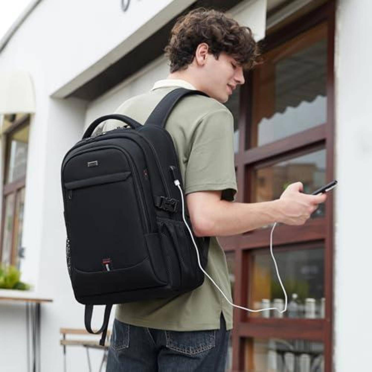 Junger Mann mit schwarzem Rucksack überprüft sein Telefon, während er vor einem Gebäude vorbeigeht.