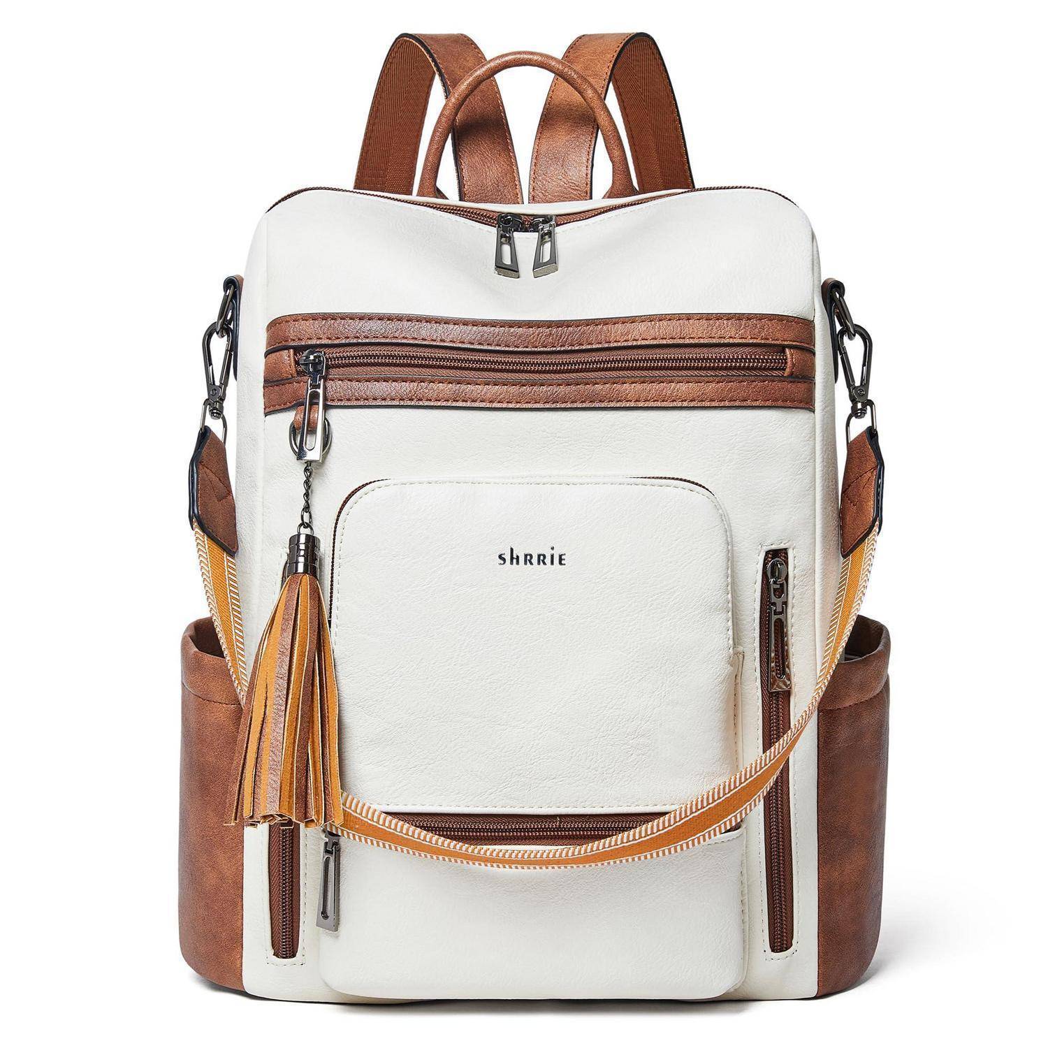 Weiß-brauner Rucksack mit vorderer Reißverschlusstasche, Quastenanhänger, Seitentaschen und Schultergurten auf schlicht strukturiertem Hintergrund.