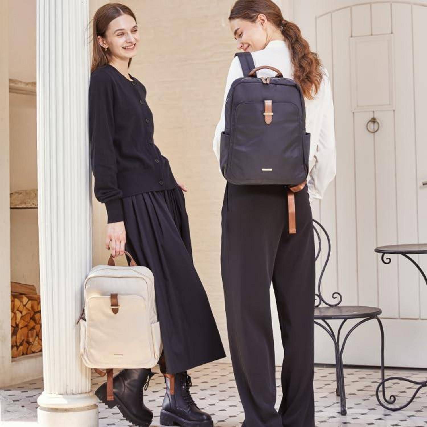 Zwei Frauen modellieren Rucksäcke: Eine hält eine cremefarbene Tasche, die andere trägt einen schwarzen Rucksack, beide in schwarzen Outfits draußen vor einer Tür.