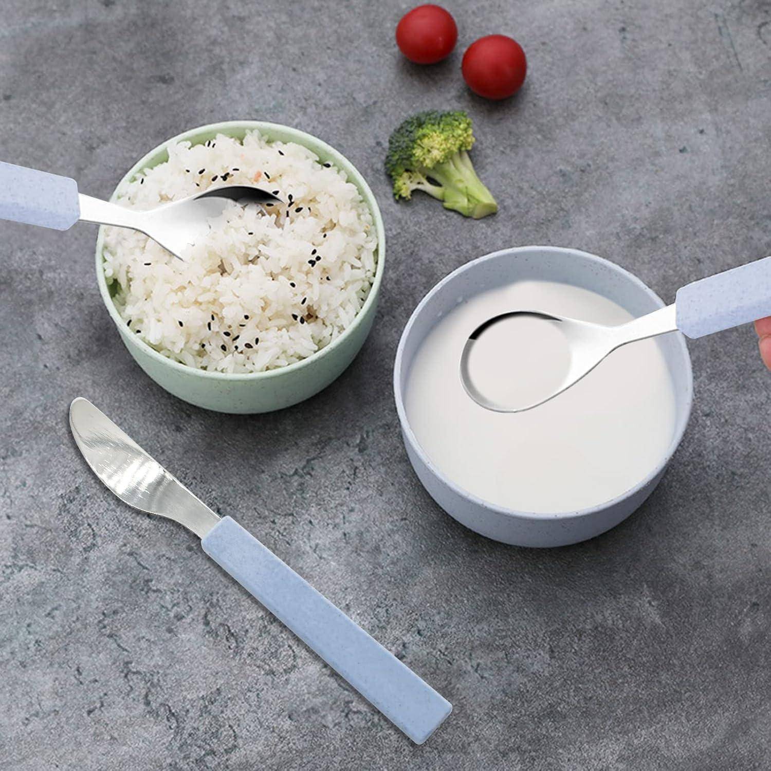 Draufsicht auf eine Reisschale und eine Suppenschale mit Löffeln, plus ein Messer, Brokkoli und zwei Kirschtomaten auf einer grauen Oberfläche.