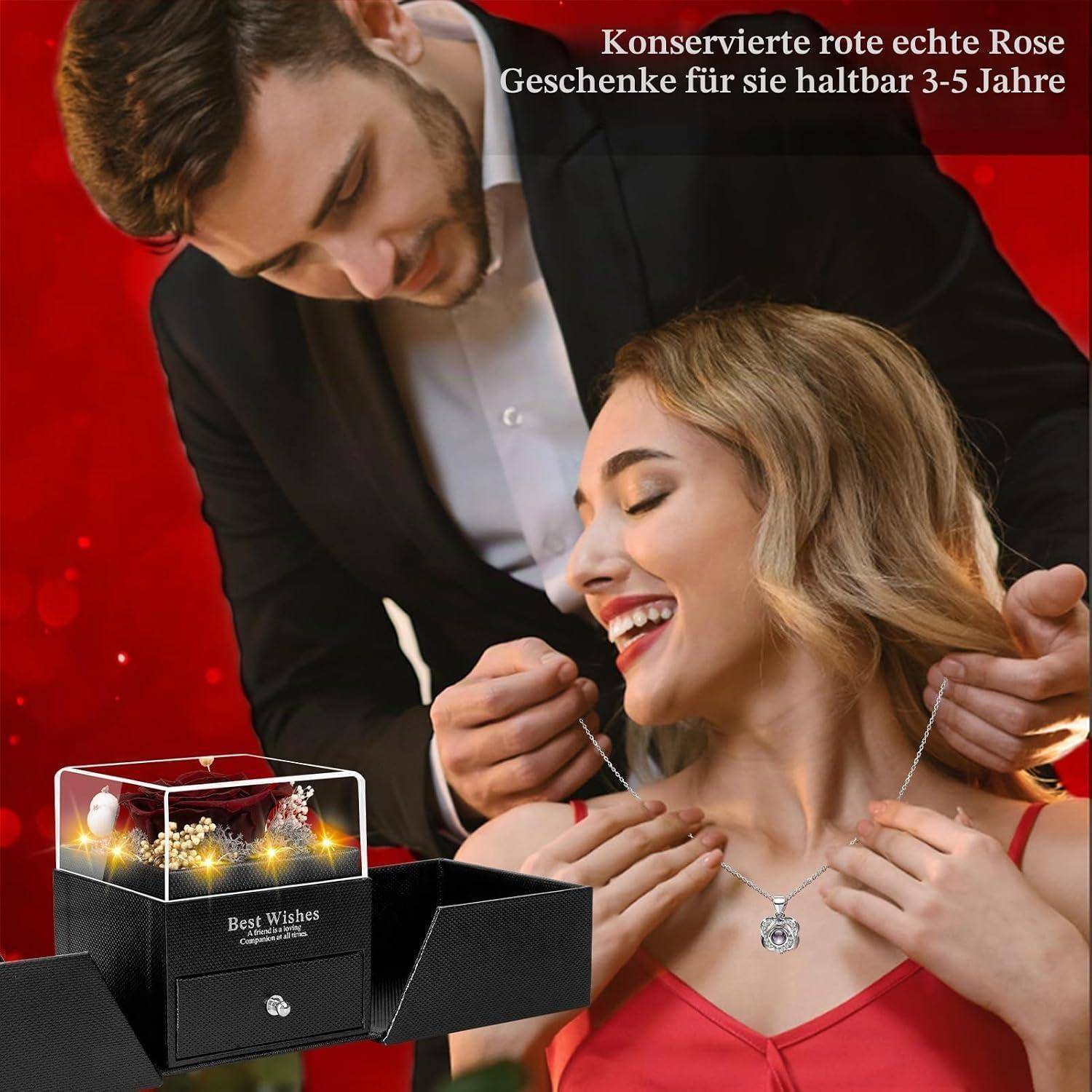 Lächelnder Mann schenkt einer Frau eine Halskette neben einer Geschenkbox mit konservierter roter Rose; der Anzeigentext lautet: „Konservierte echte rote Rosen als Geschenk für sie, hält 3-5 Jahre