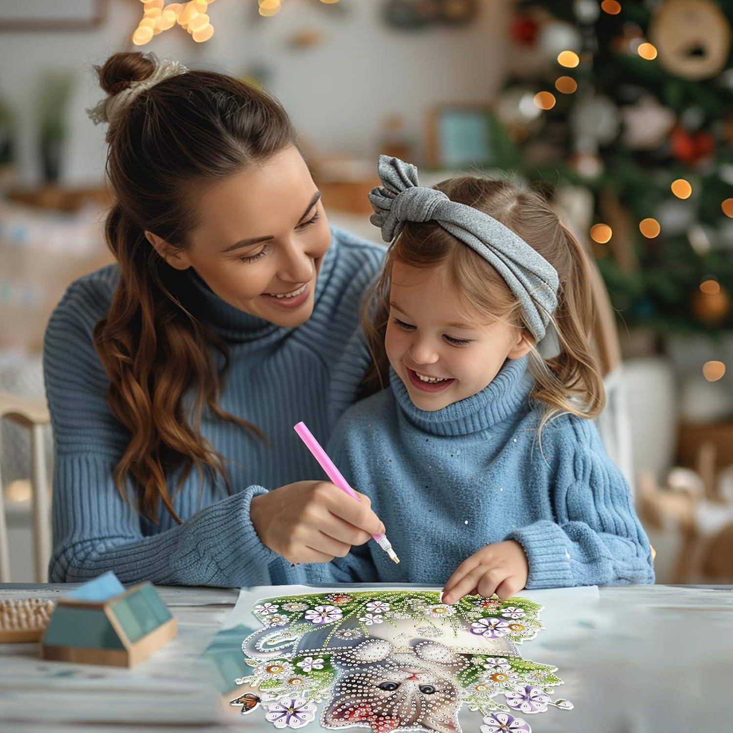 Mutter hilft ihrer kleinen Tochter, ein Blumen-Welpen-Bild an einem Tisch auszumalen, mit einem geschmückten Weihnachtsbaum im Hintergrund.