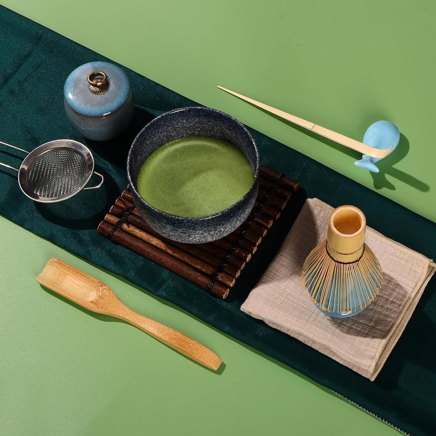 Matcha-Tee-Set mit einer Schale grünem Tee, Schneebesen, Sieb, Löffel und zwei kleinen Behältern auf einem Tablett.