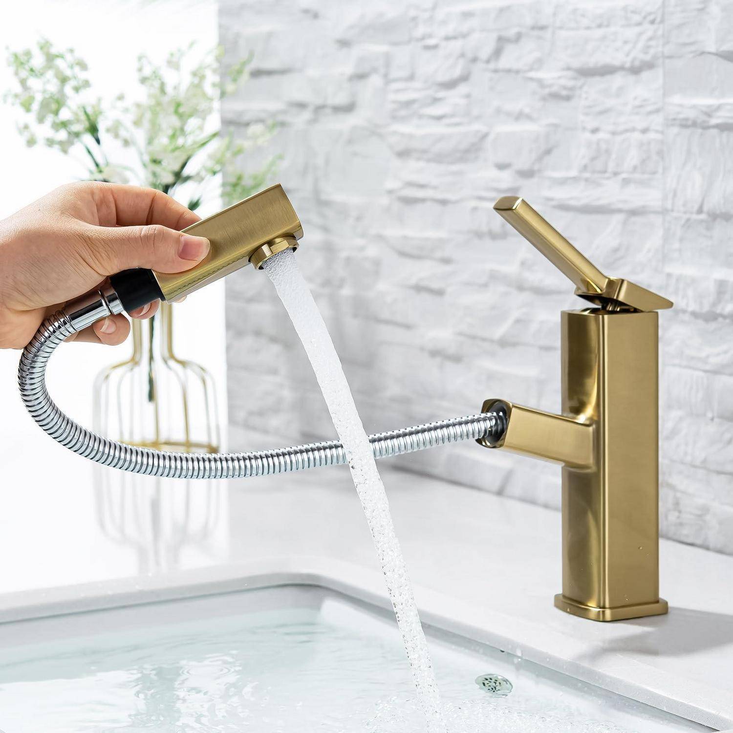 Eine Hand hält einen goldenen tragbaren Sprüher über einem Badezimmerspülbecken, wobei Wasser aus der Düse neben einem passenden goldenen Wasserhahn fließt.