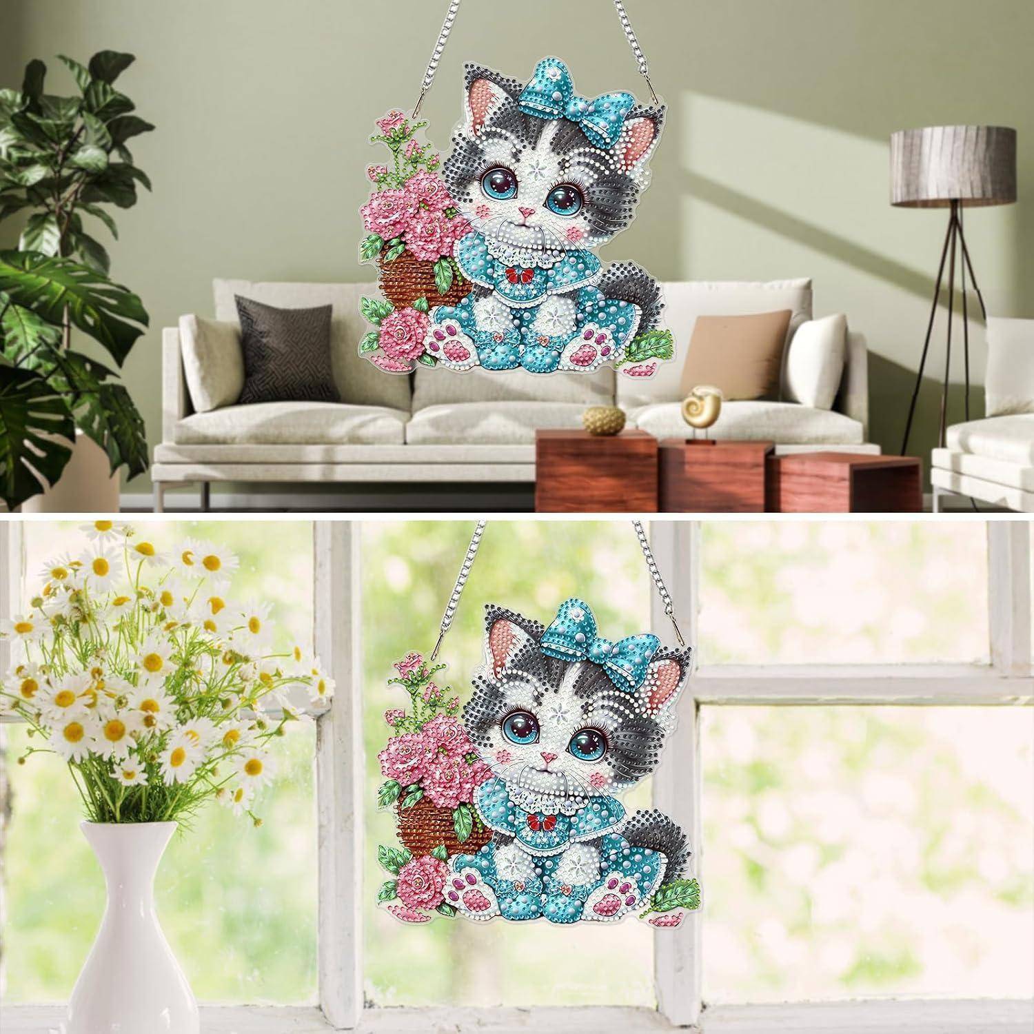 Ein glitzerndes katzenförmiges Wandornament zum Aufhängen mit einer blauen Schleife und rosa Blumen, das in einem Wohnzimmer und an einem Fenster präsentiert wird.