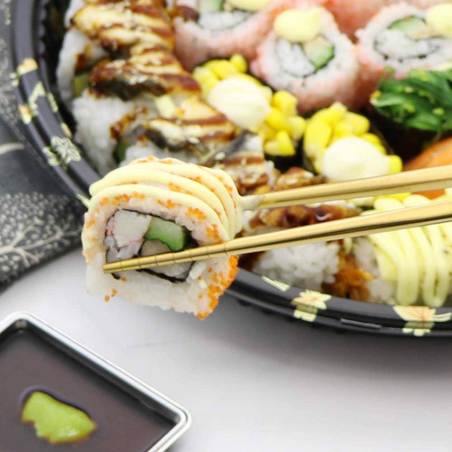 Essstäbchen heben eine Sushi-Rolle von einem Tablett mit sortiertem Sushi und Saucen auf einem Tisch.