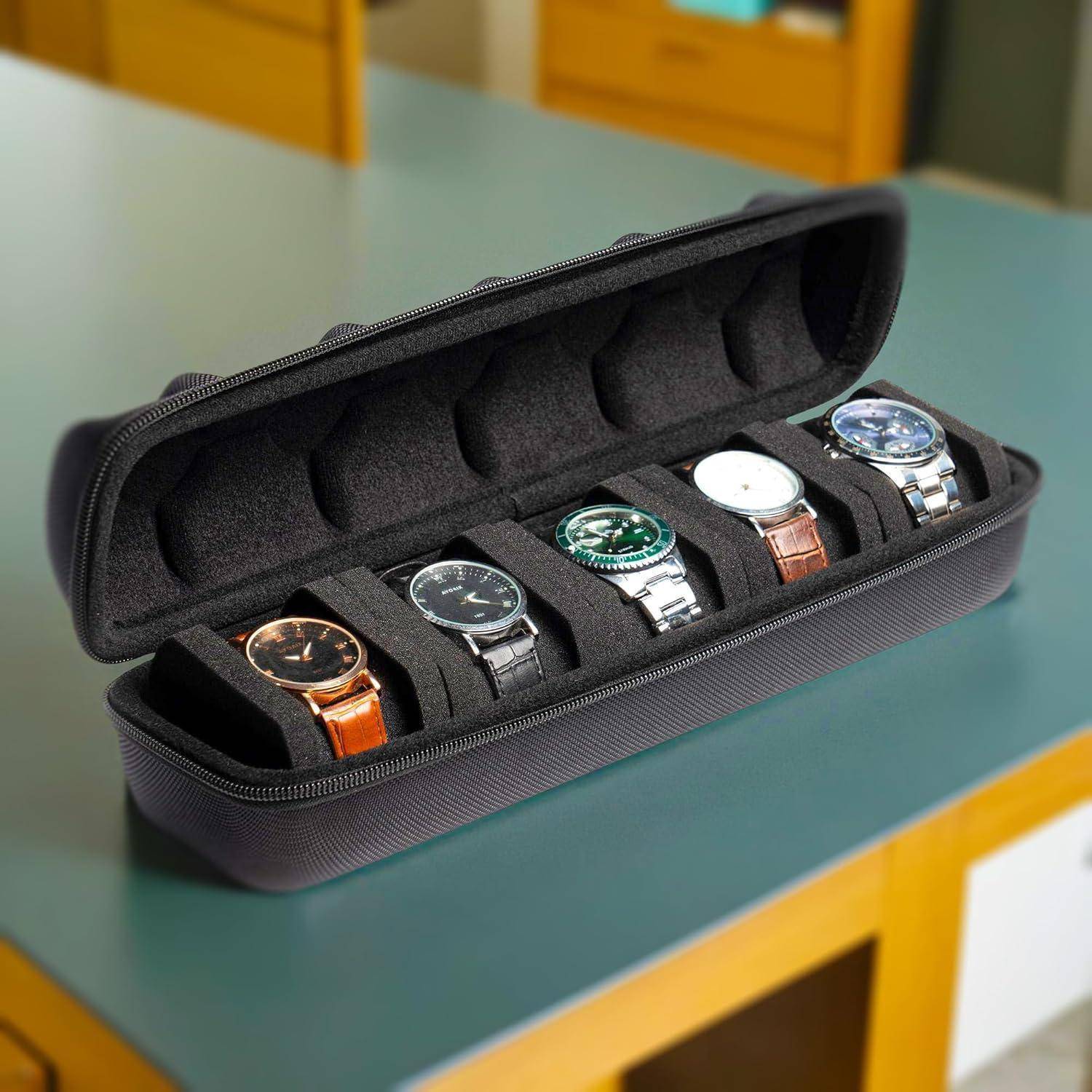 Offene schwarze Uhrenreiseetui mit fünf Armbanduhren in einzelnen Schaumstoffaussparungen auf einem Tisch.