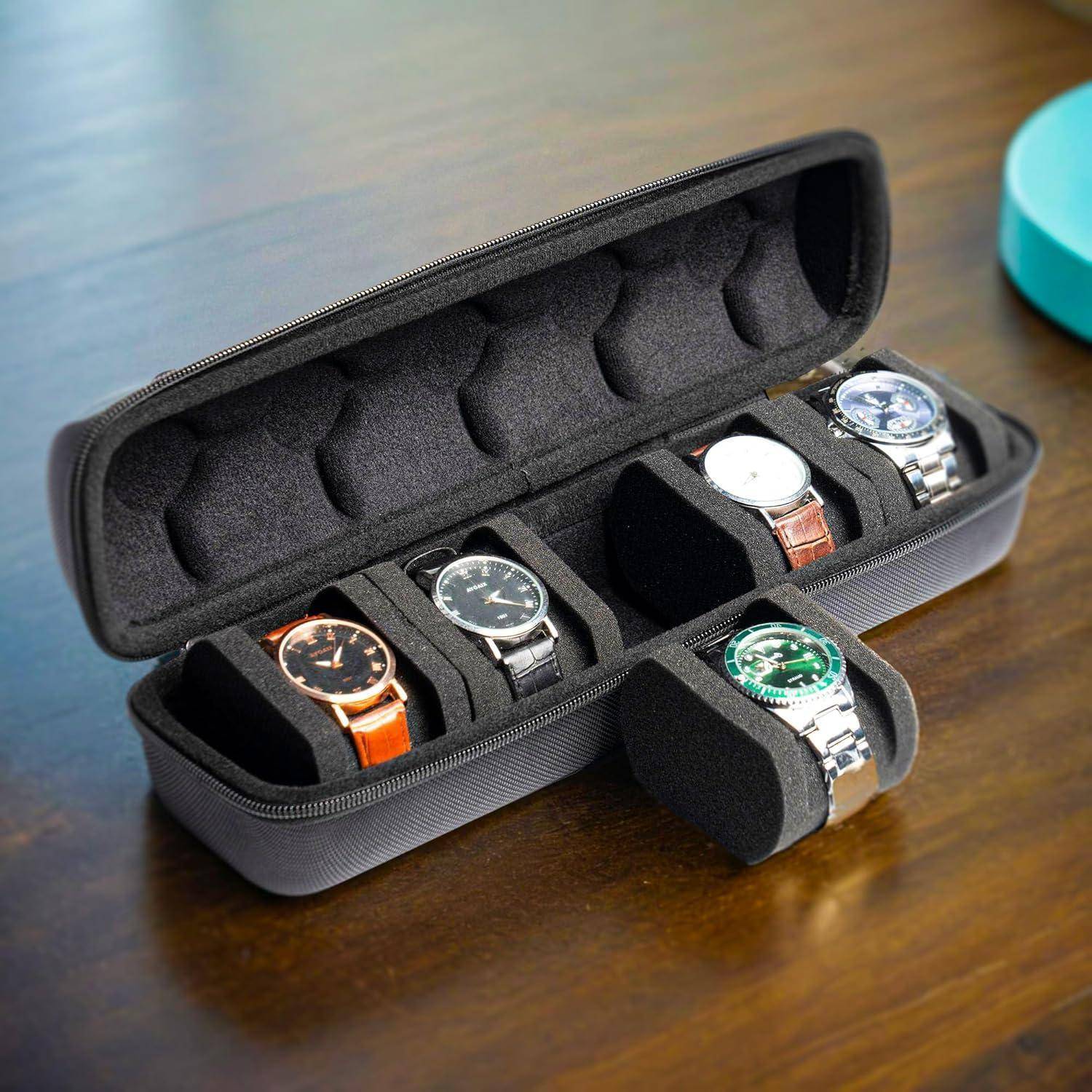Offene Uhrenaufbewahrungsbox auf einem Tisch, die vier Armbanduhren in Schaumstoffnischen hält.