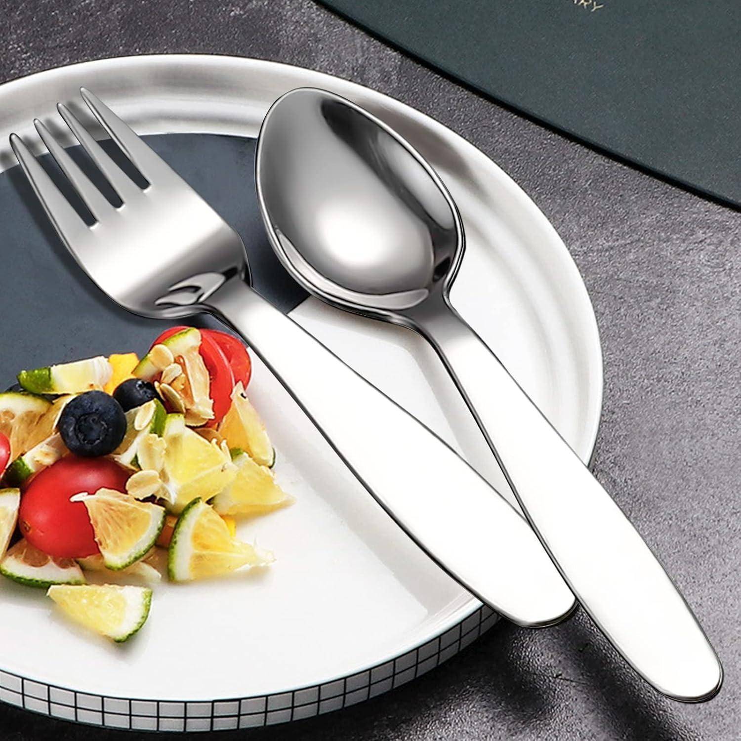 Silberne Gabel und Löffel auf einem weißen Teller neben einem kleinen Fruchtsalat auf einem grauen Tisch.