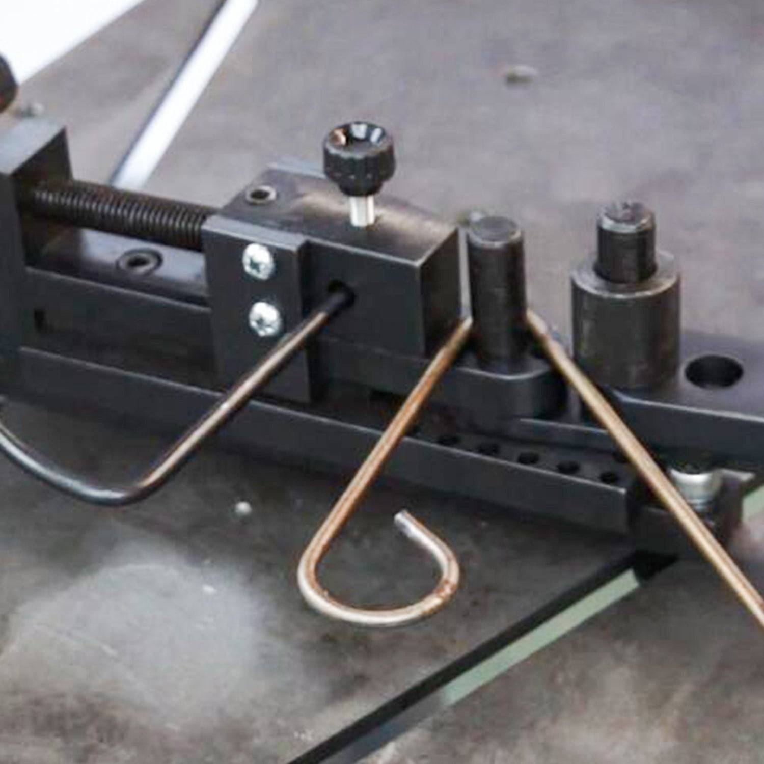 Nahaufnahme einer Metallbiegemaschine mit drei gebogenen Drahtbügeln, die auf einer Werkbank eingespannt sind.