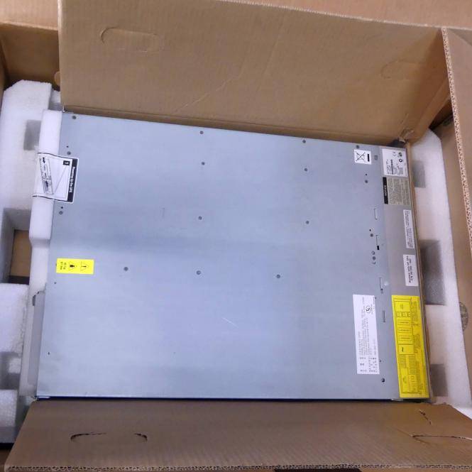 Eine große flache silberne Metall-Elektronikeinheit, verpackt in einem Kartonversandkarton mit Schaumstoffeinlagen und Warnkennzeichnungen.