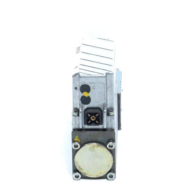 Nahaufnahme einer kleinen elektronischen/mechanischen Komponente mit metallischem Gehäuse, Anschlussanschluss und runder Kappe an der Vorderseite, dargestellt vor weißem Hintergrund.