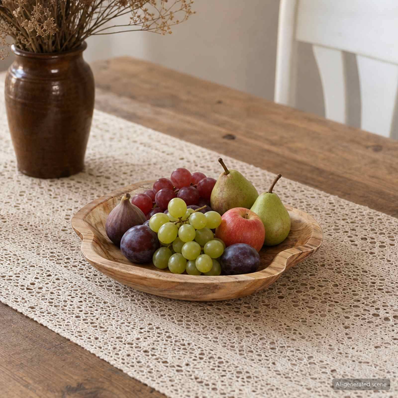 Holzschale mit gemischtem Obst – grüne und rote Trauben, Birnen, Feigen und ein Apfel – auf einem Spitzenläufer auf einem rustikalen Tisch arrangiert.