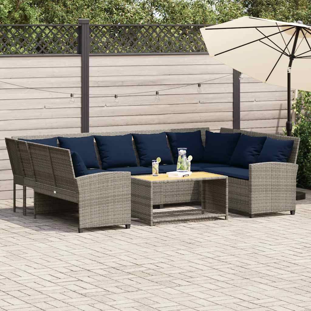 Outdoor-Sitzbereich auf der Terrasse mit einem grauen Rattan-Ecksofa, dunklen Kissen, niedrigem Tisch und Sonnenschirm auf einer gepflasterten Terrasse.