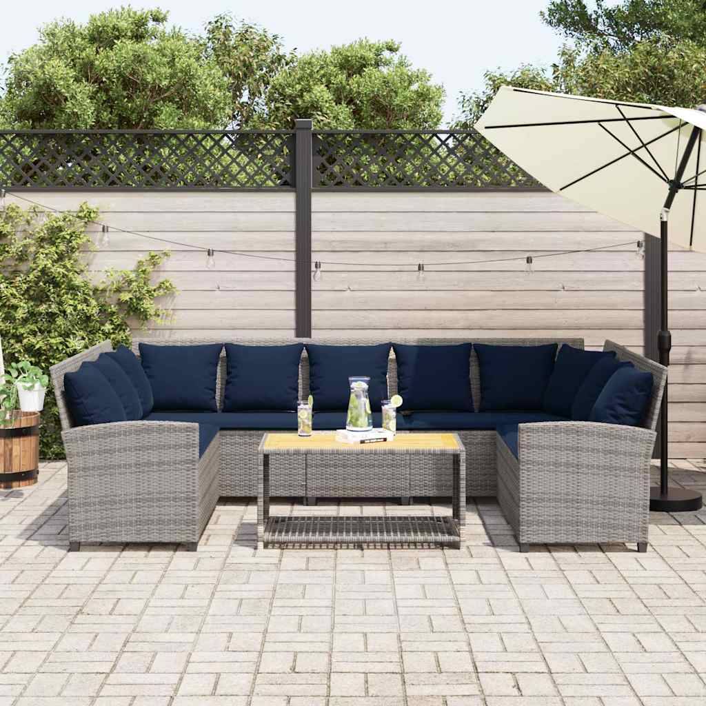 Außenbereich mit Terrassensitzgruppe mit grauem Polyrattan-Ecksofa, dunkelblauem Kissen, Couchtisch und Sonnenschirm neben einem Holzzaun und einer Topfpflanze.
