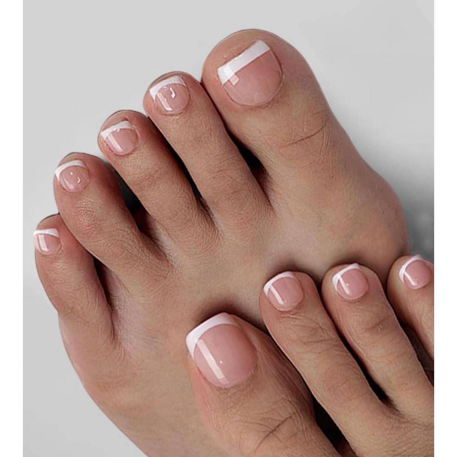 Nahaufnahme von zwei Füßen mit sorgfältig manikürierten Zehennägeln, die in zartem Rosa mit weißen French-Tips lackiert sind, auf hellgrauem Hintergrund.
