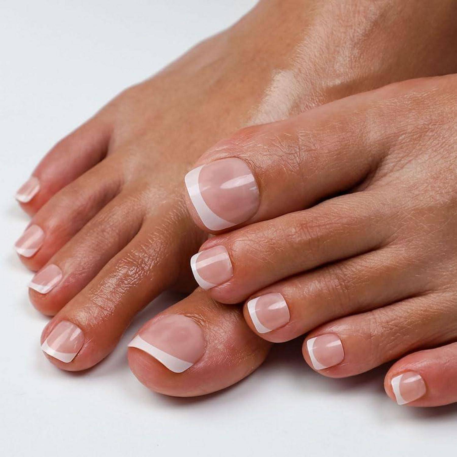 Nahaufnahme von gepflegten Fußnägeln mit klarem Lack und weißen French-Nails auf weißem Hintergrund.