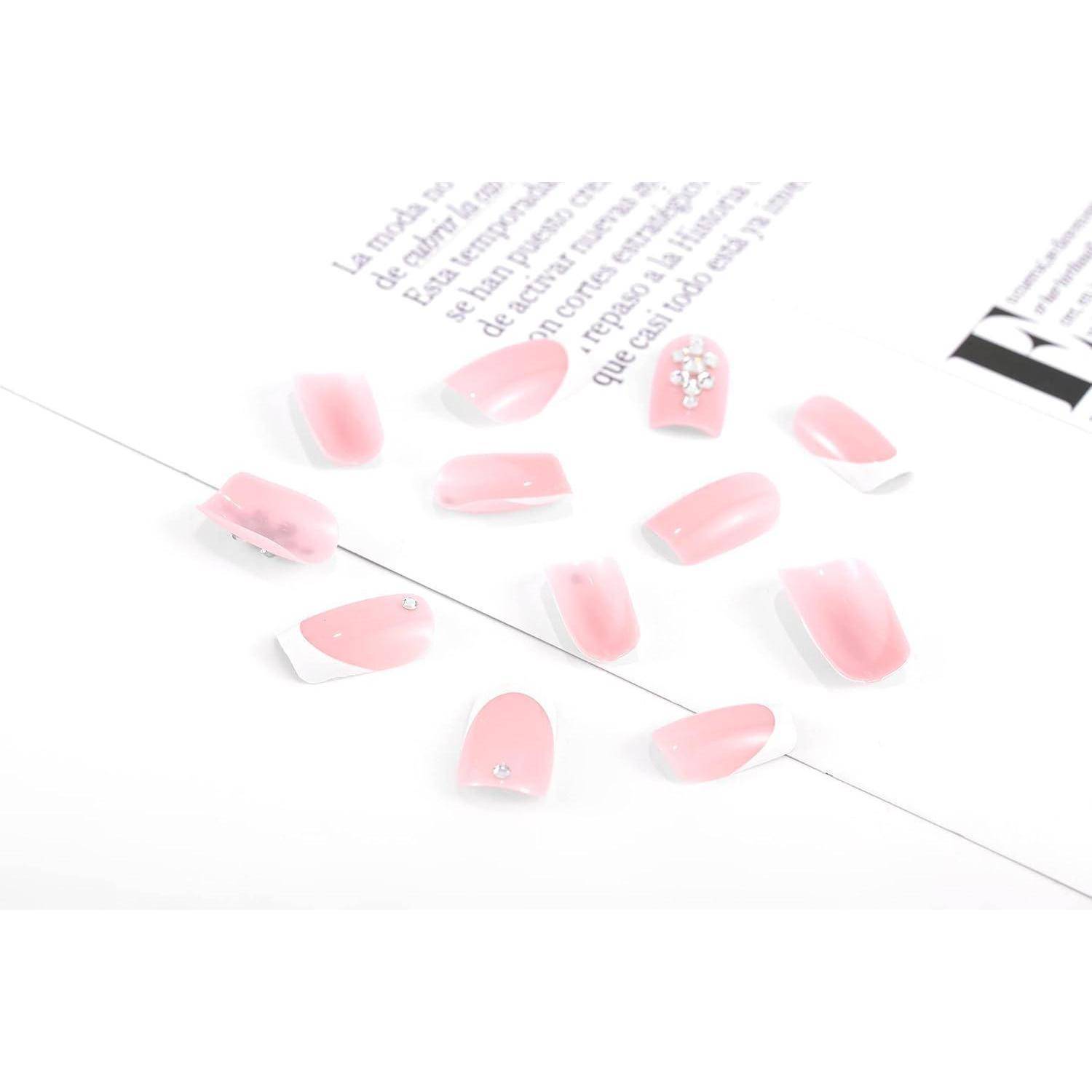 Rosa künstliche Nageldesigns auf weißem Hintergrund angeordnet, mit einem Nagel, der mit kleinen Rhinestenen verziert ist und schwachem bedrucktem Text darüber.
