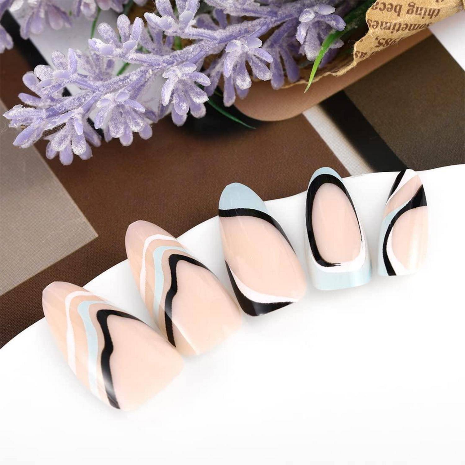 Fünf künstliche Nagelspitzen mit abstrakten schwarzen, weißen und beigen Wellendesigns auf einer weißen Ausstellungsfläche angeordnet, mit violetten Blumen im Hintergrund.