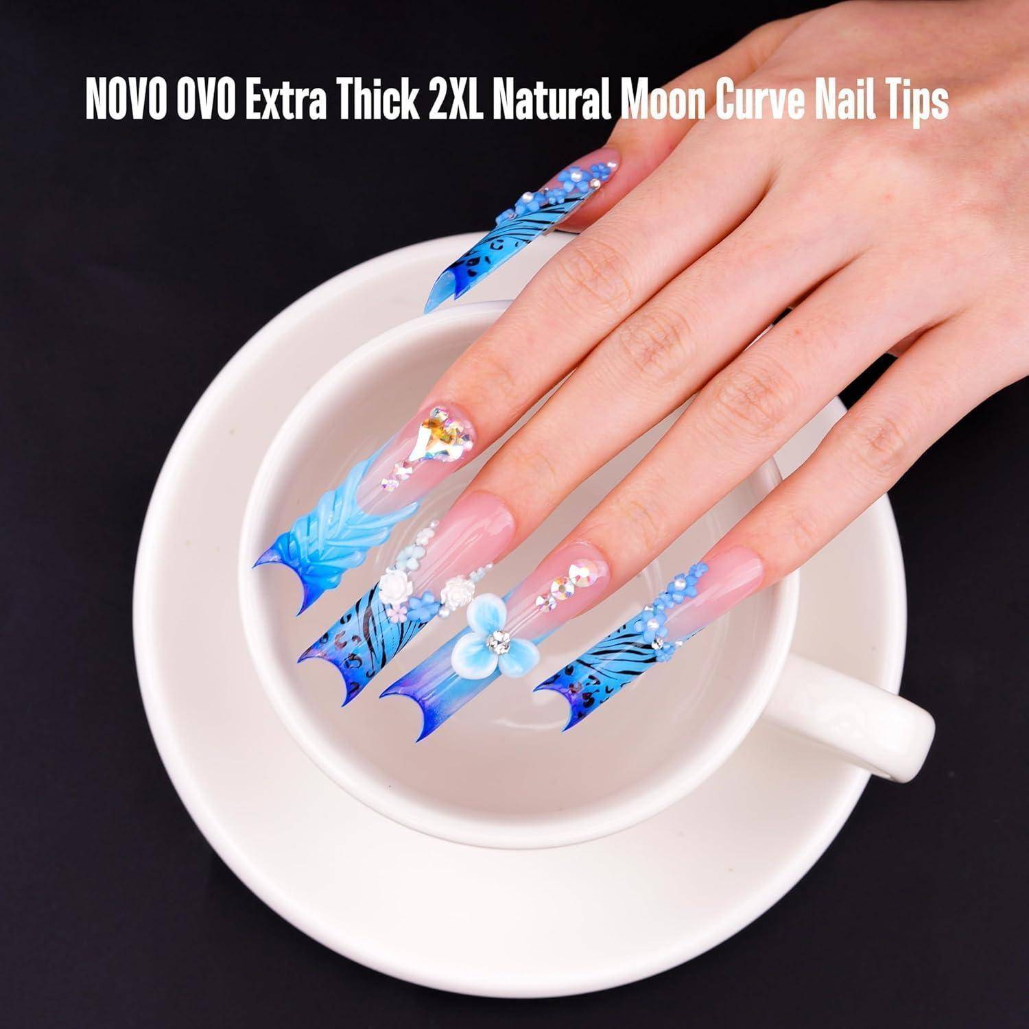 Hand mit langen blauen blumigen Nagelspitzen, die über eine weiße Tasse und Untertasse gehalten werden, beschriftet mit „NOVO OVO Extra Thick 2XL Natural Moon Curve Nail Tips