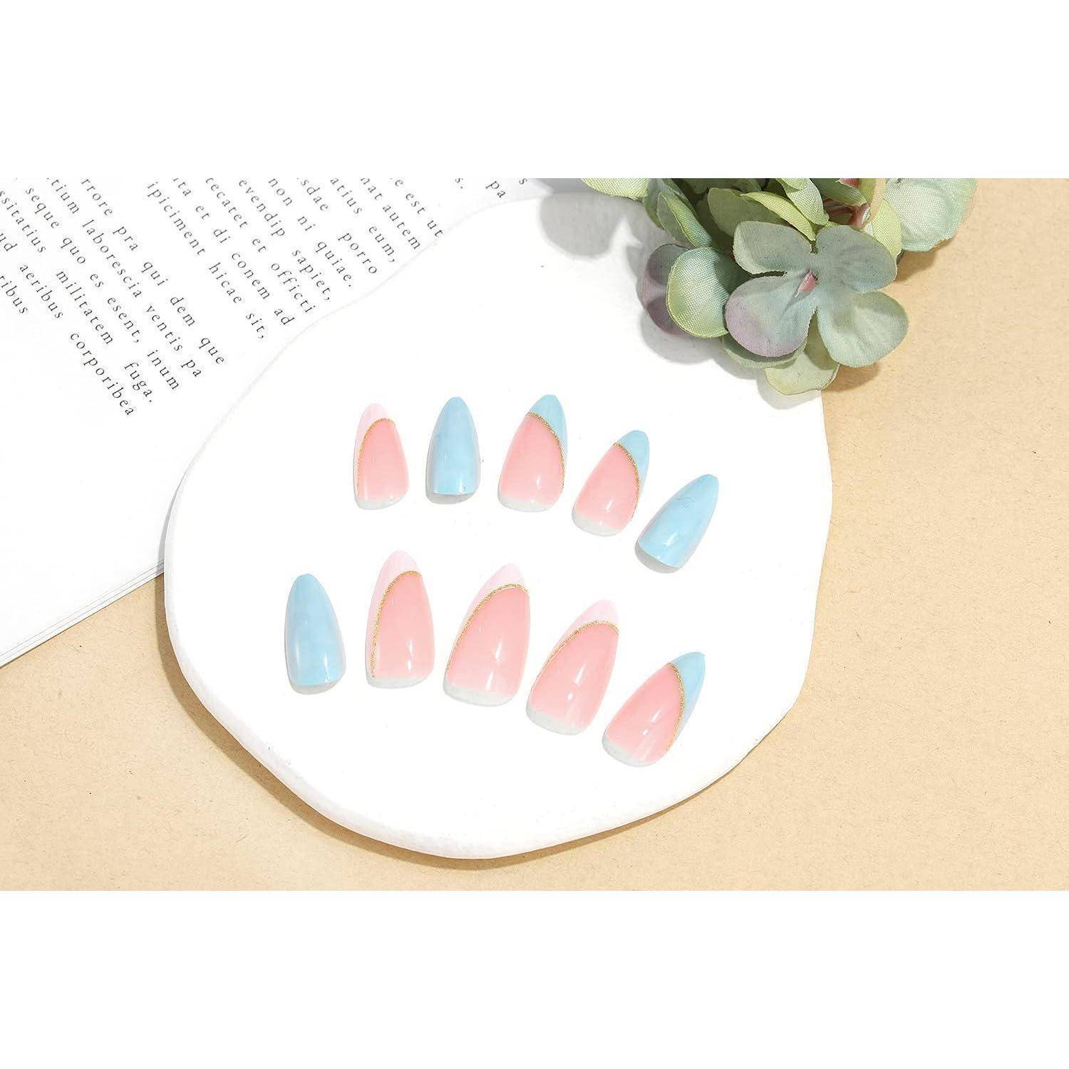Pastellrosa und hellblaue künstliche Nagelspitzen, die auf einem weißen Displayteller angeordnet sind, mit einer kleinen Sukkulente und einem aufgeschlagenen Buch in der Nähe.