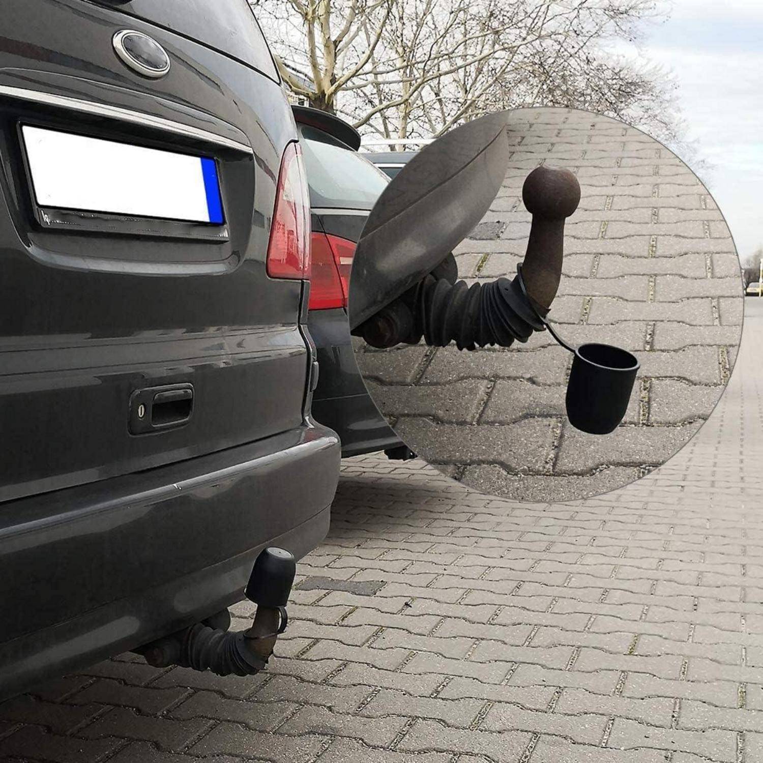 Hinterseite eines SUV mit einer Anhängekupplung und einer abgedeckten Anhängersteckdose; die vergrößerte Nahaufnahme zeigt eine baumelnde Schutzkappe am Kupplungsstecker.
