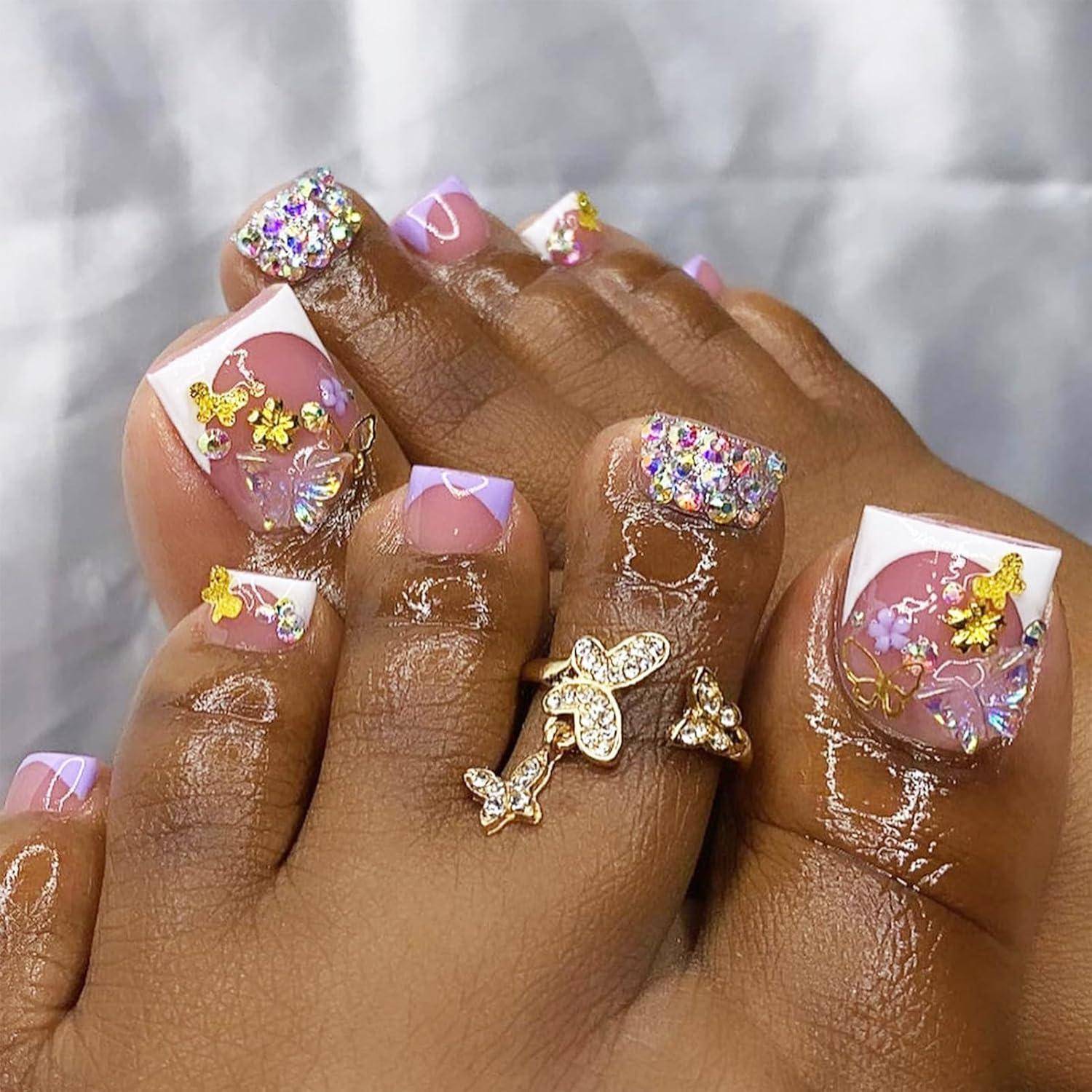 Nahaufnahme von Füßen mit glänzender rosa-weißer französischer Pediküre, Schmetterlings-Nagelkunst, Glitzereffekten und goldenen Zehrenringen.