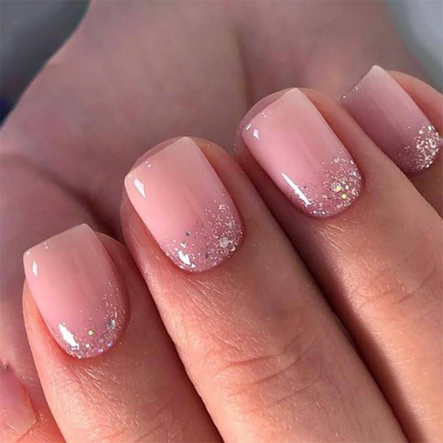 Nahaufnahme von maniküren Fingernägeln mit glänzendem hellrosa Nagellack und glitzernden silbernen Ombré-Spitzen.