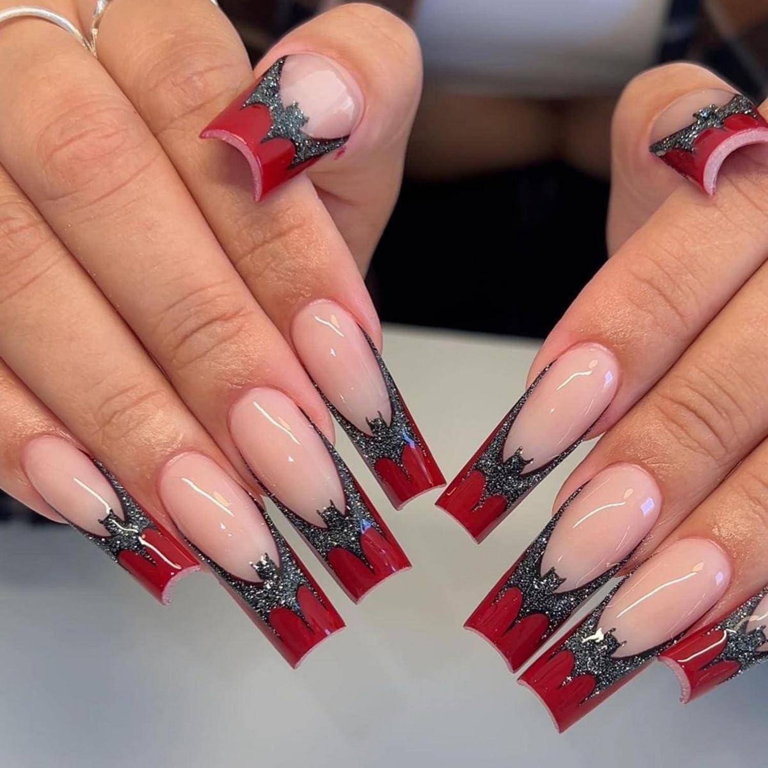 Hände mit langen, nackten Nägeln mit roten French-Tip-Spitzen und schwarzen Glitter-Starburst-Akzenten.