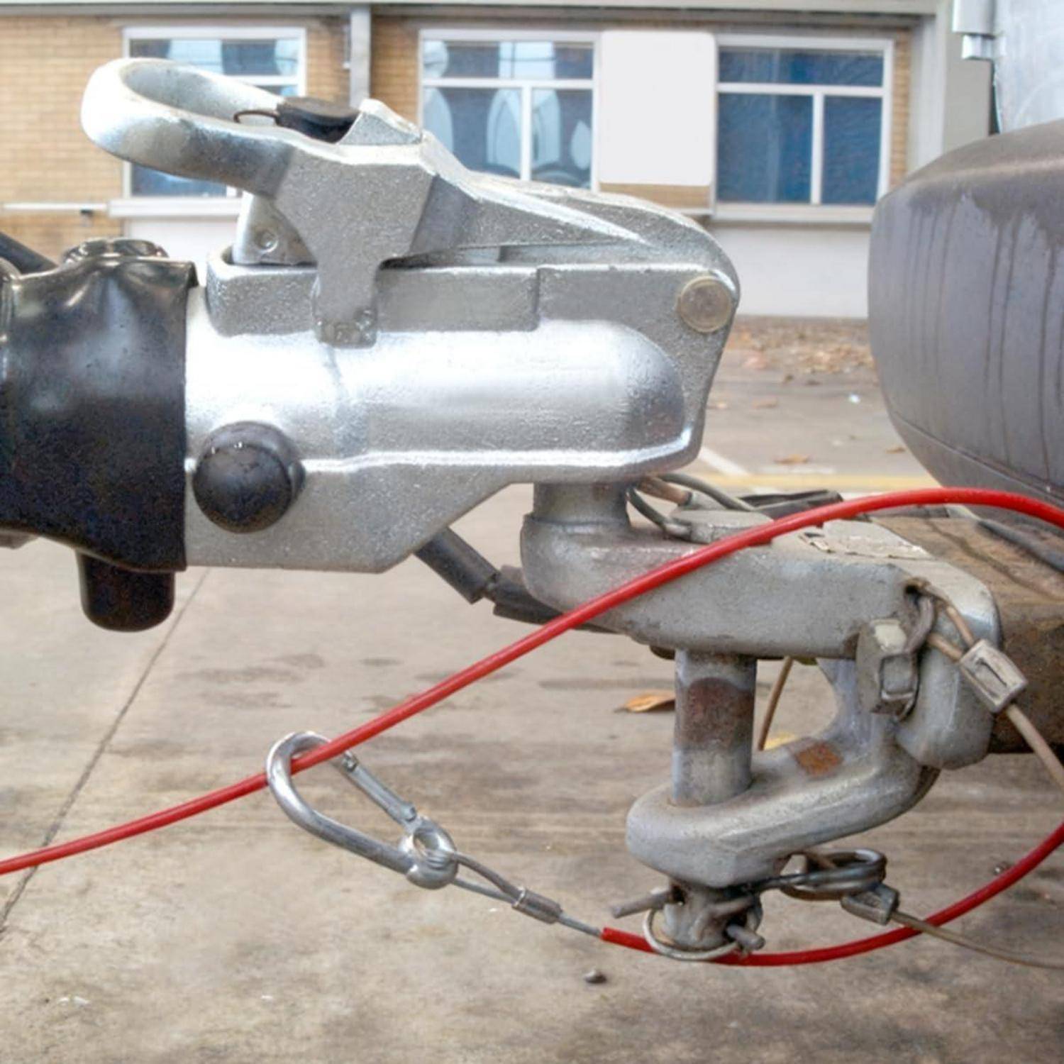 Nahaufnahme einer Anhängerkupplung, die an einem Zugfahrzeug befestigt ist, mit einem roten Sicherheitsseil und einer Metallkette auf einer Auffahrt.