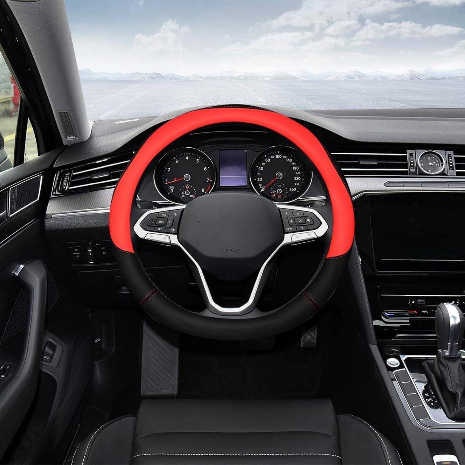 Blick vom Fahrersitz auf ein modernes Autoinnenraum, das ein rot-schwarzes Lenkrad, Armaturenbrettinstrumente, Mitteldisplay und Schalthebel zeigt.