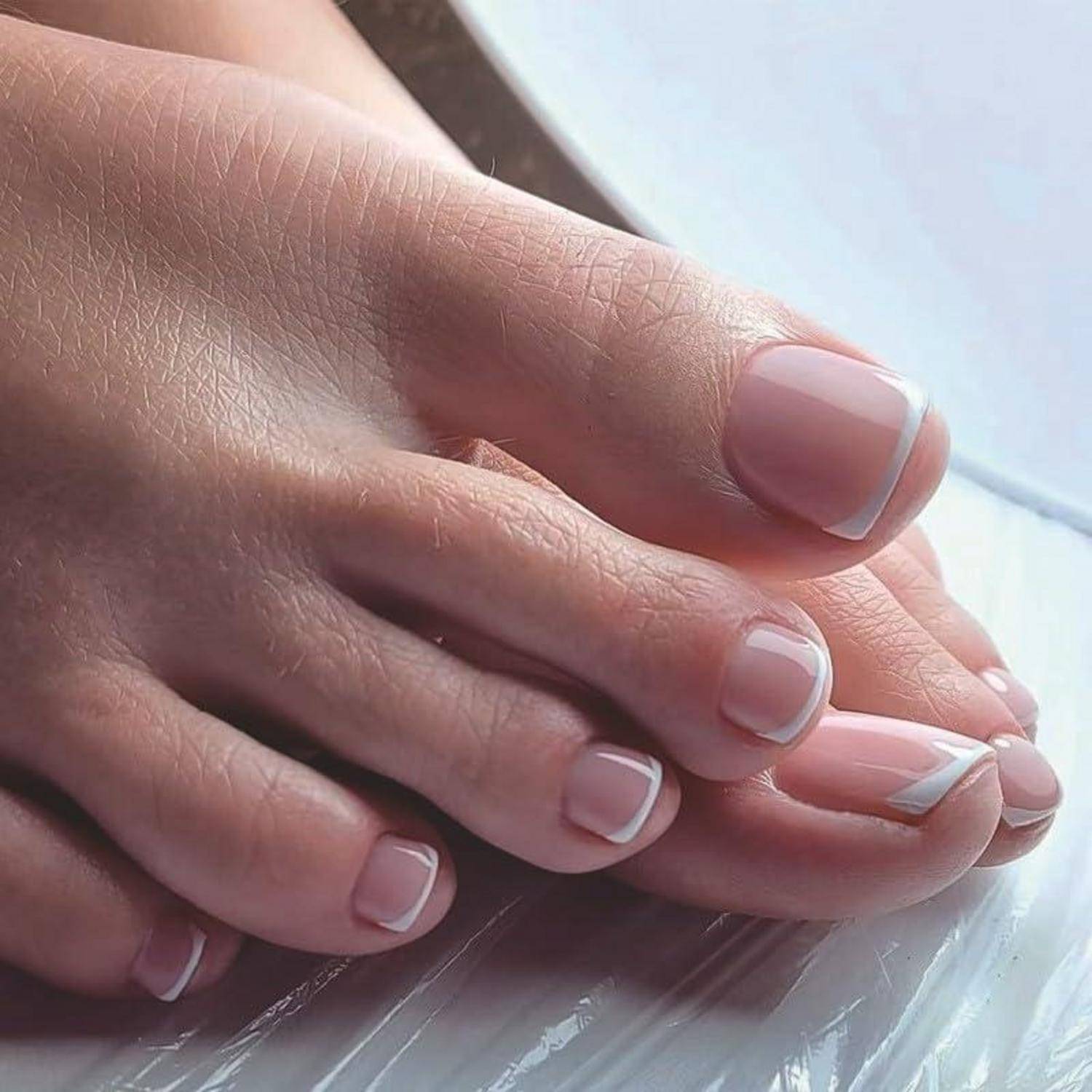 Nahaufnahme von Füßen mit ordnungsgemäß pediküren Zehen, die mit zartem Rosa und weißen French-Tips lackiert sind und auf einer hellen Oberfläche ruhen.