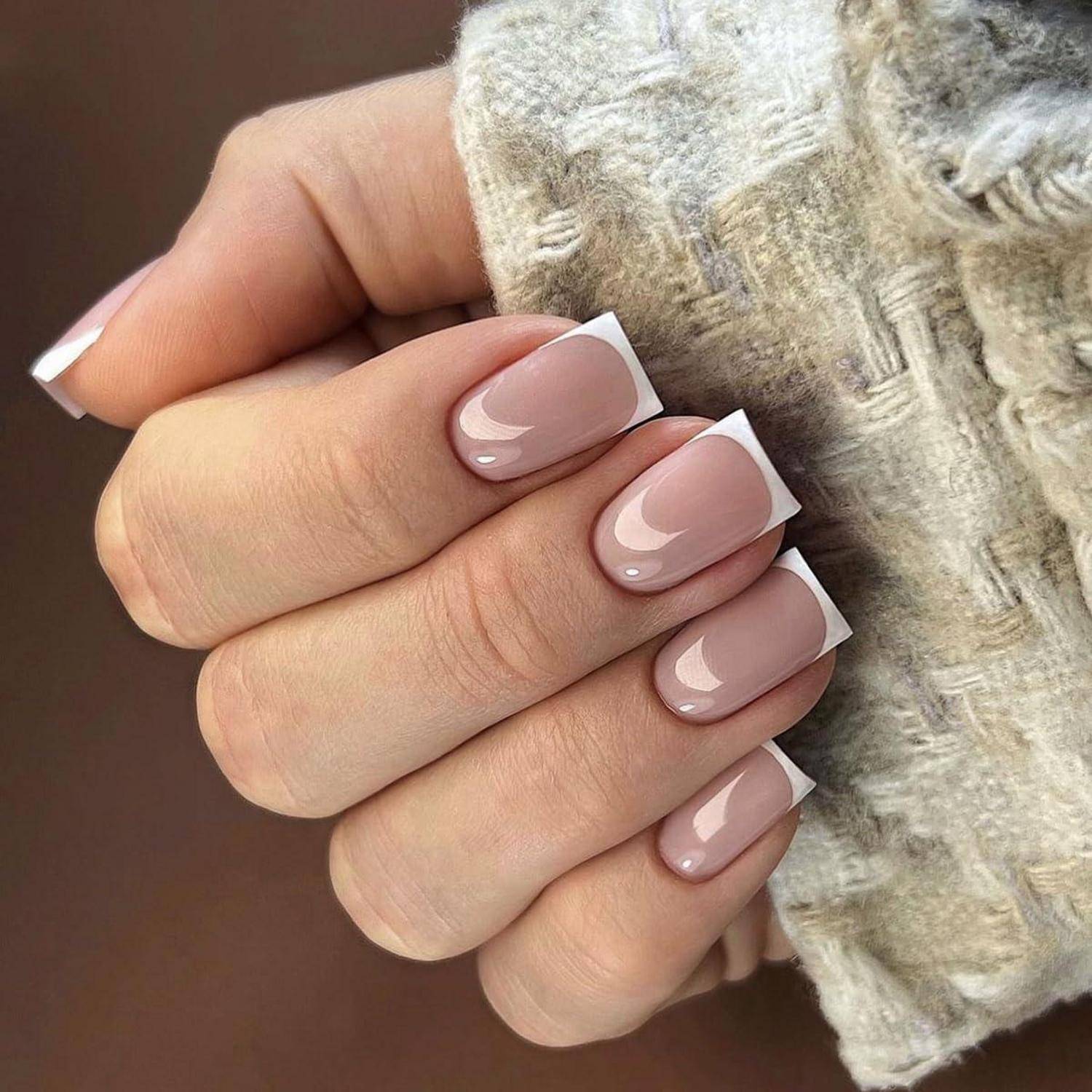 Nahaufnahme einer Hand mit glänzender nackter French Manicure und kurzen quadratischen Nägeln, die einen weichen beigen Stoff hält.