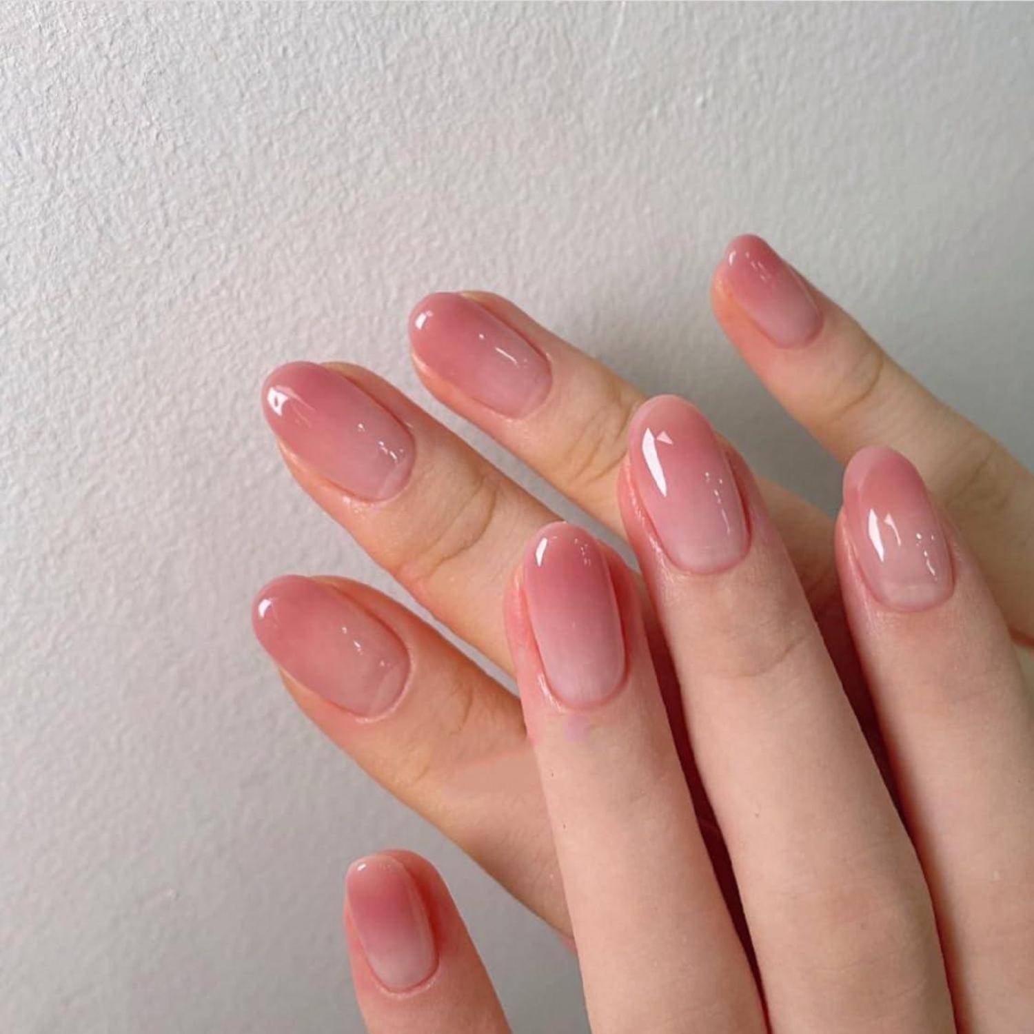 Nahaufnahme von zwei Händen mit langen, glänzend rosa manikürten Nägeln vor einer schlichten, hellen Wand.
