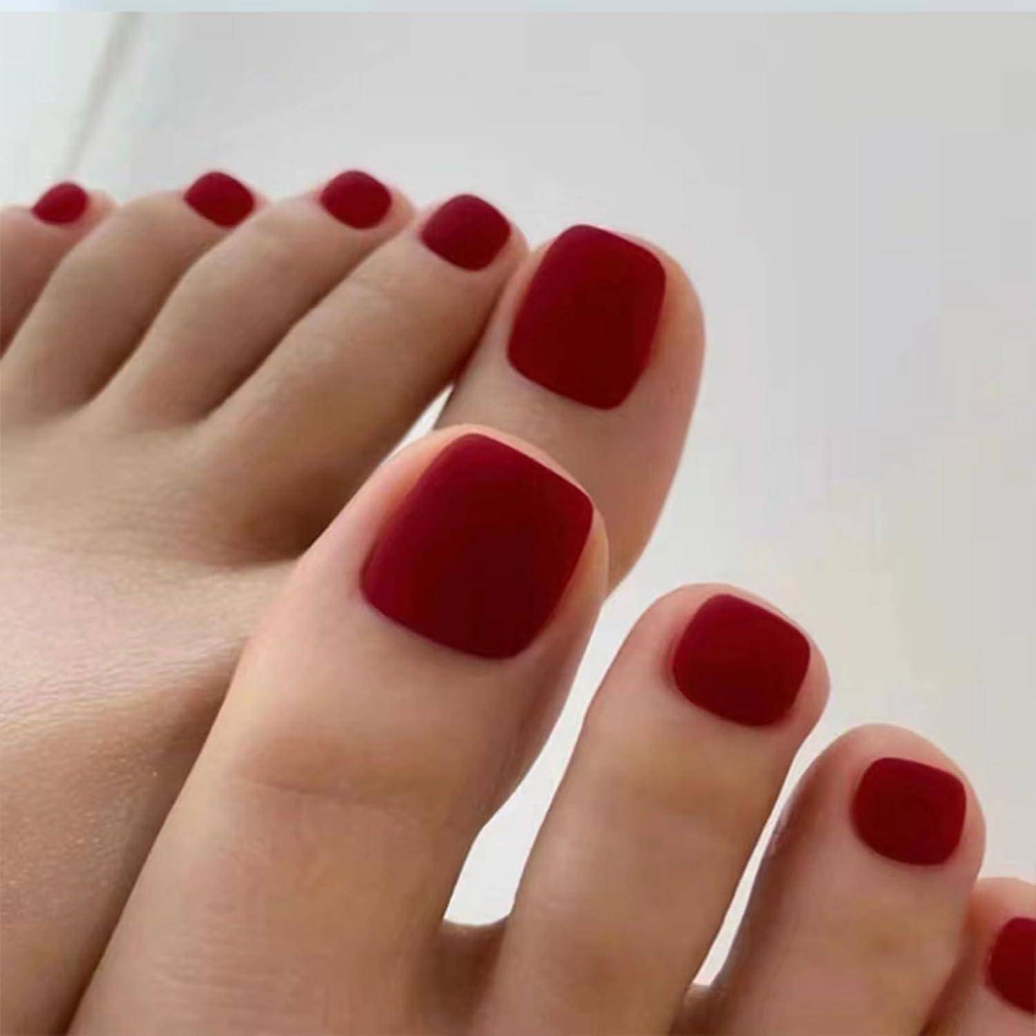 Nahaufnahme von Zehen mit glänzendem dunkelrotem Nagellack auf einem Fuß mit heller Hautfarbe vor einem einfachen Hintergrund.