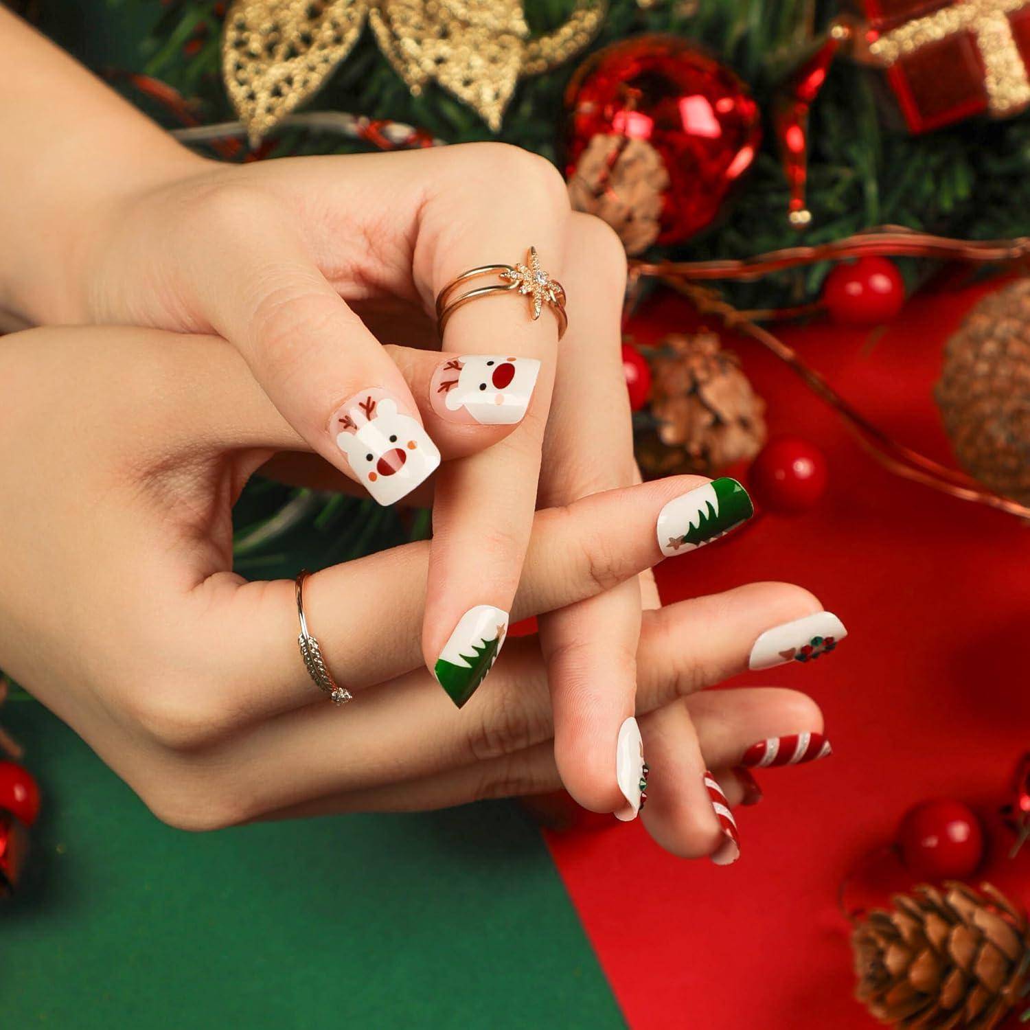 Hände mit Weihnachts-Nagelkunst und Ringen, die über einem rot-grünen Feiertagshintergrund mit Ornamenten und Tannenzapfen posiert sind.