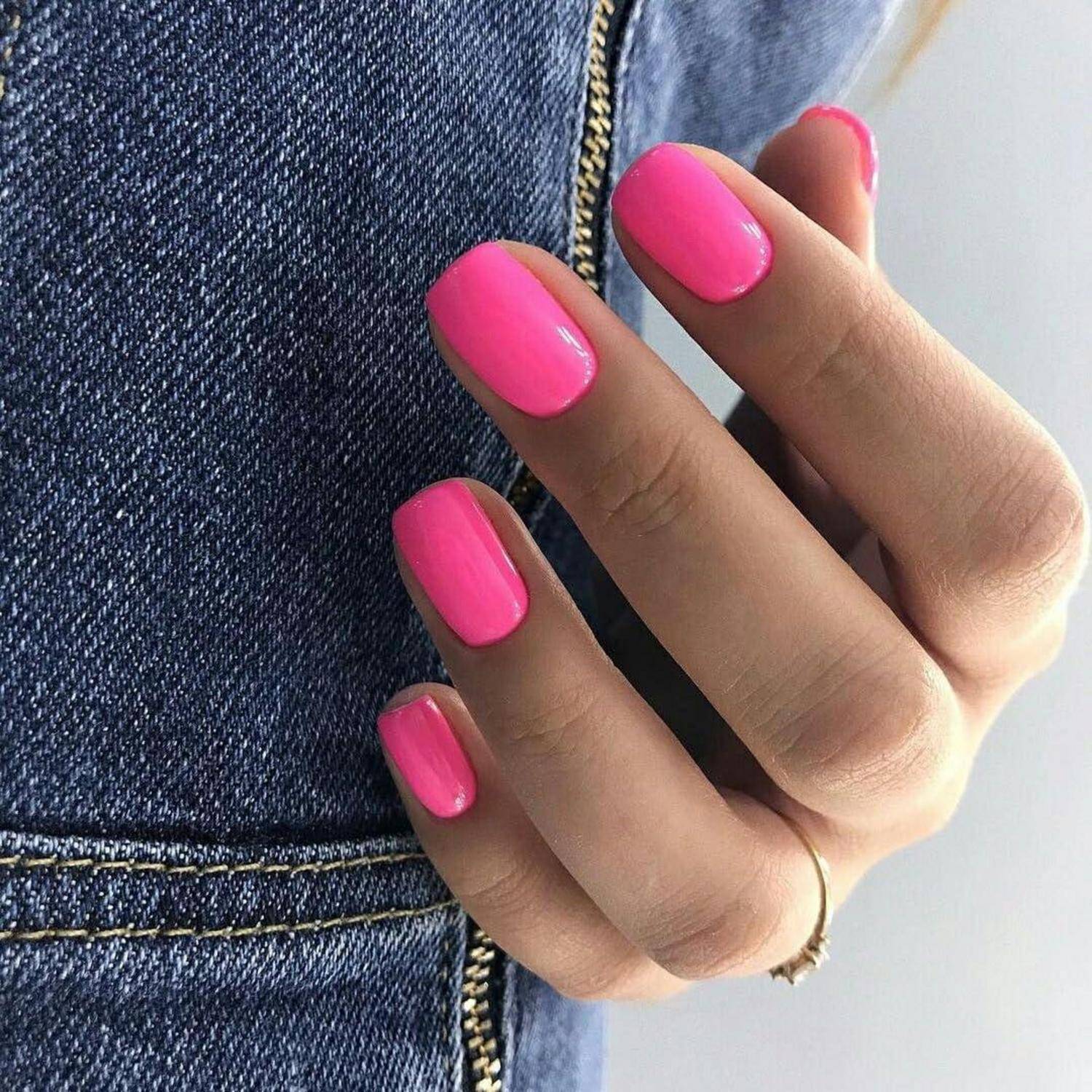 Nahaufnahme einer Hand mit leuchtend rosa maniküerten Nägeln vor einer Jeanshose.