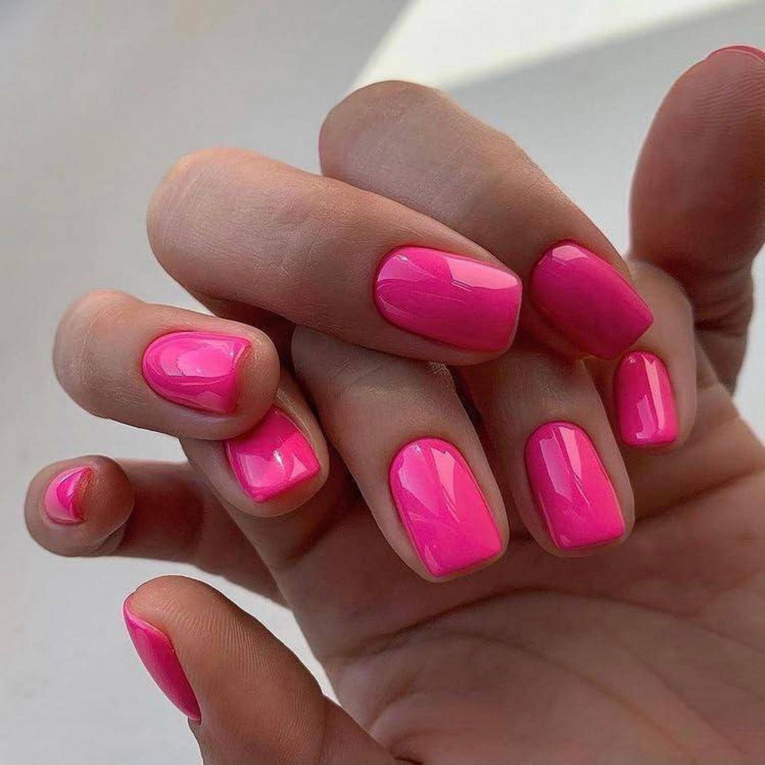 Nahaufnahme von Händen mit glänzenden, leuchtend rosa manikürierten Nägeln.